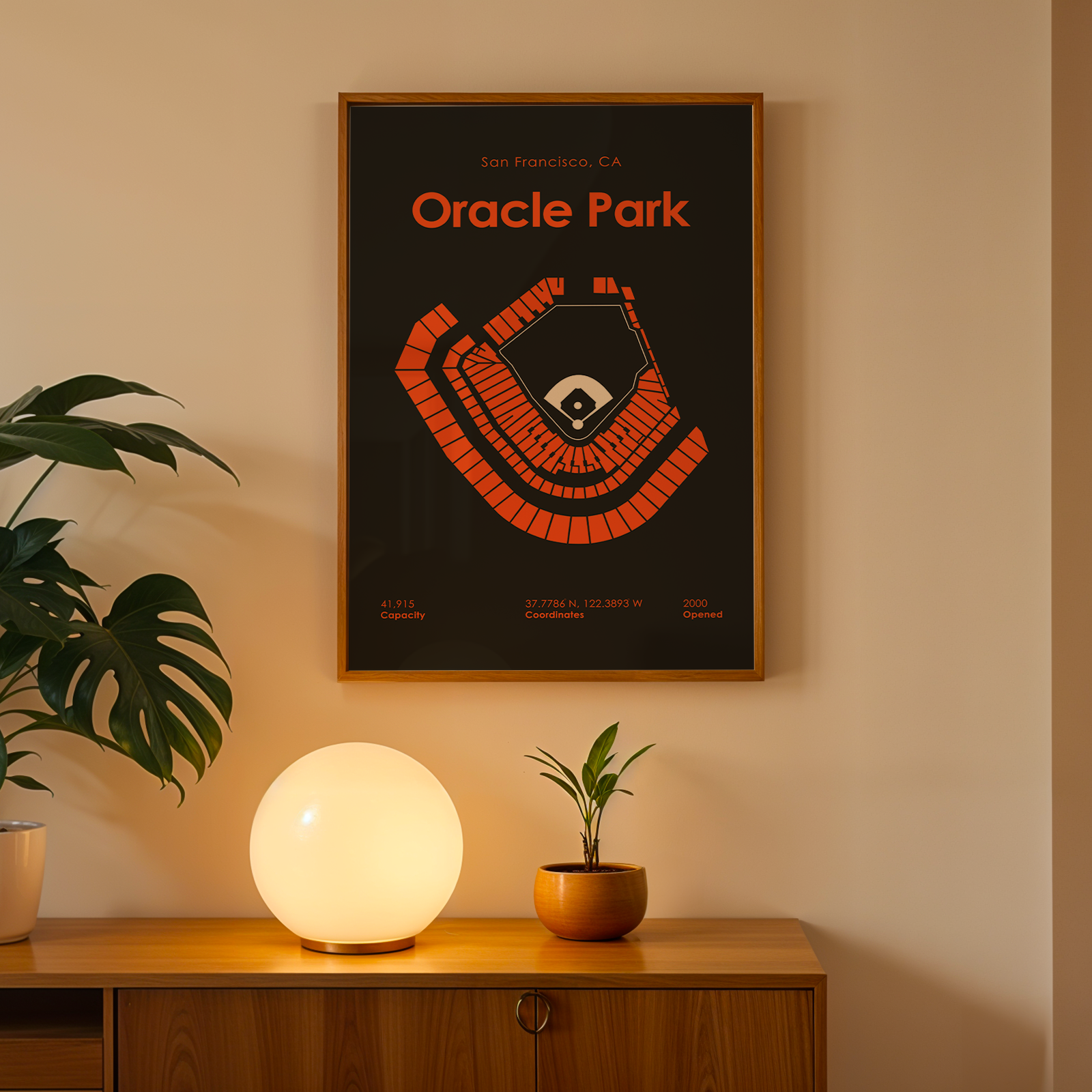 Framed poster of Oracle Park on a wall above a wooden cabinet with a lamp and plant.