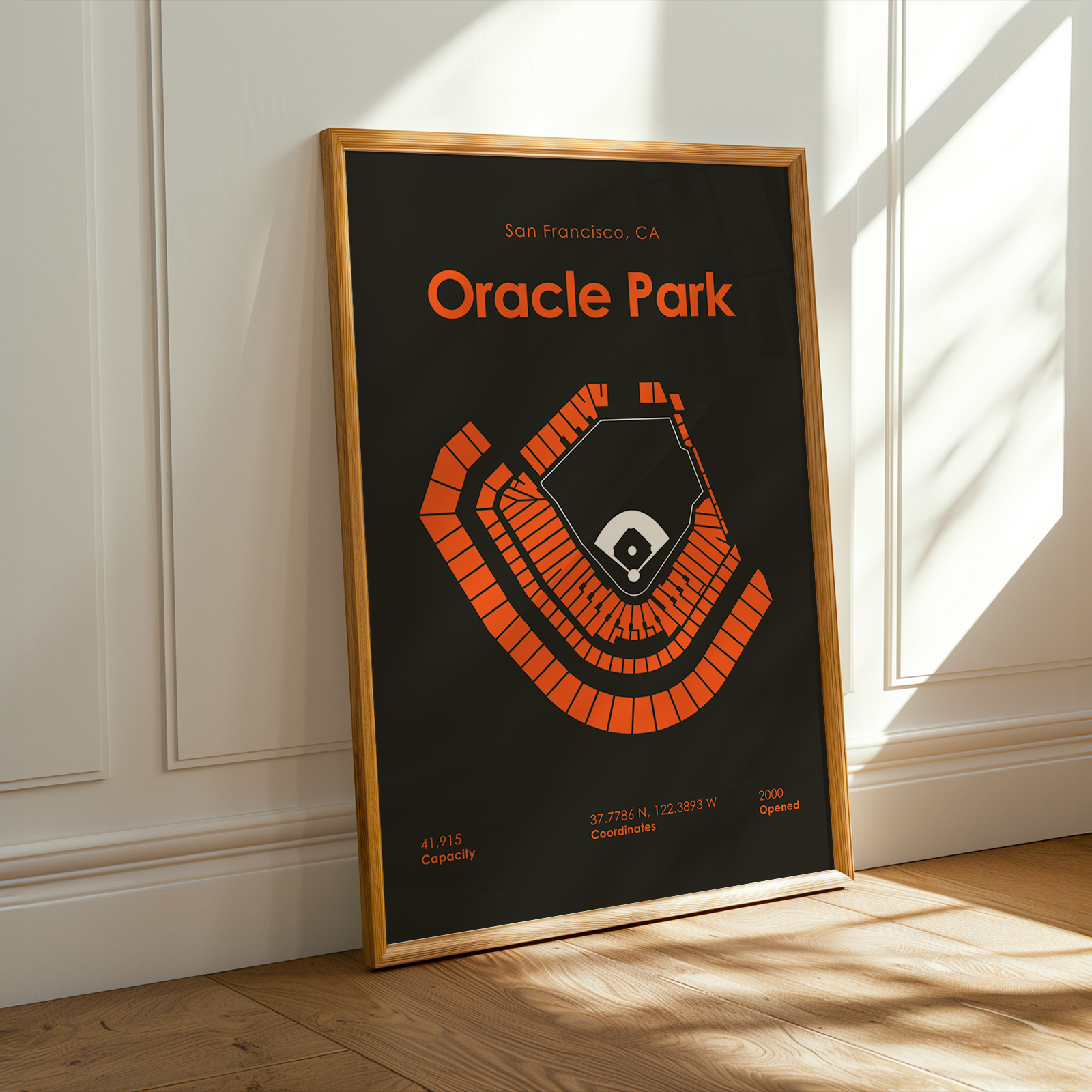 Framed poster of Oracle Park with orange text on a black background, leaning against a white wall.