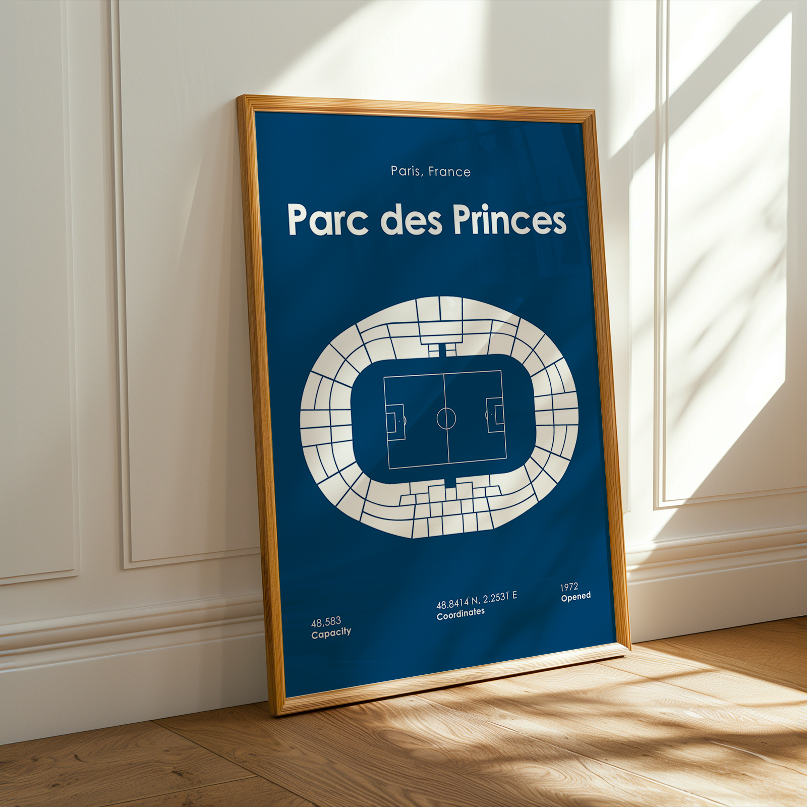 Framed poster of Parc des Princes stadium layout on a blue background, leaning against a white wall.