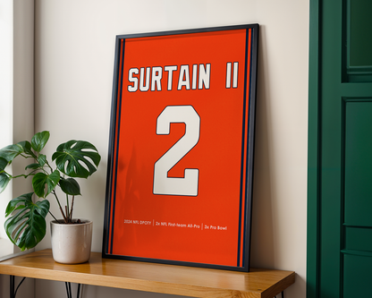 Framed sports jersey with 'Surtain II' and number '2' on an orange background, placed on a wooden surface.