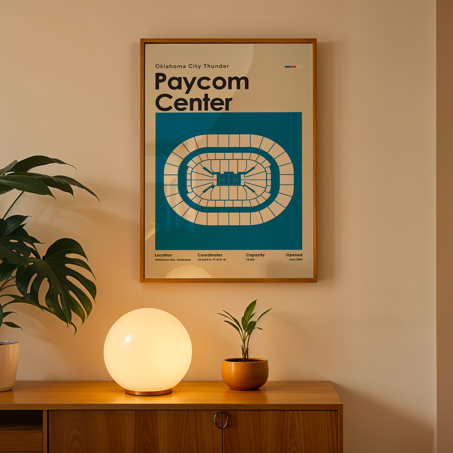 Framed poster of Paycom Center on a wall above a wooden cabinet with decorative items.