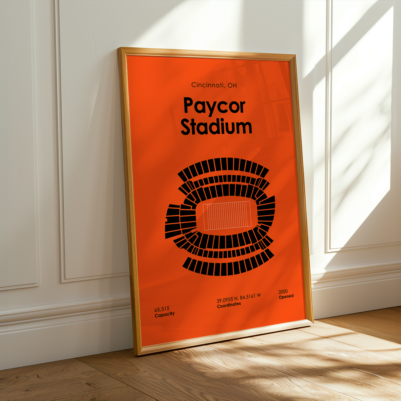 Framed poster of Paycor Stadium on a wall with sunlight casting shadows.