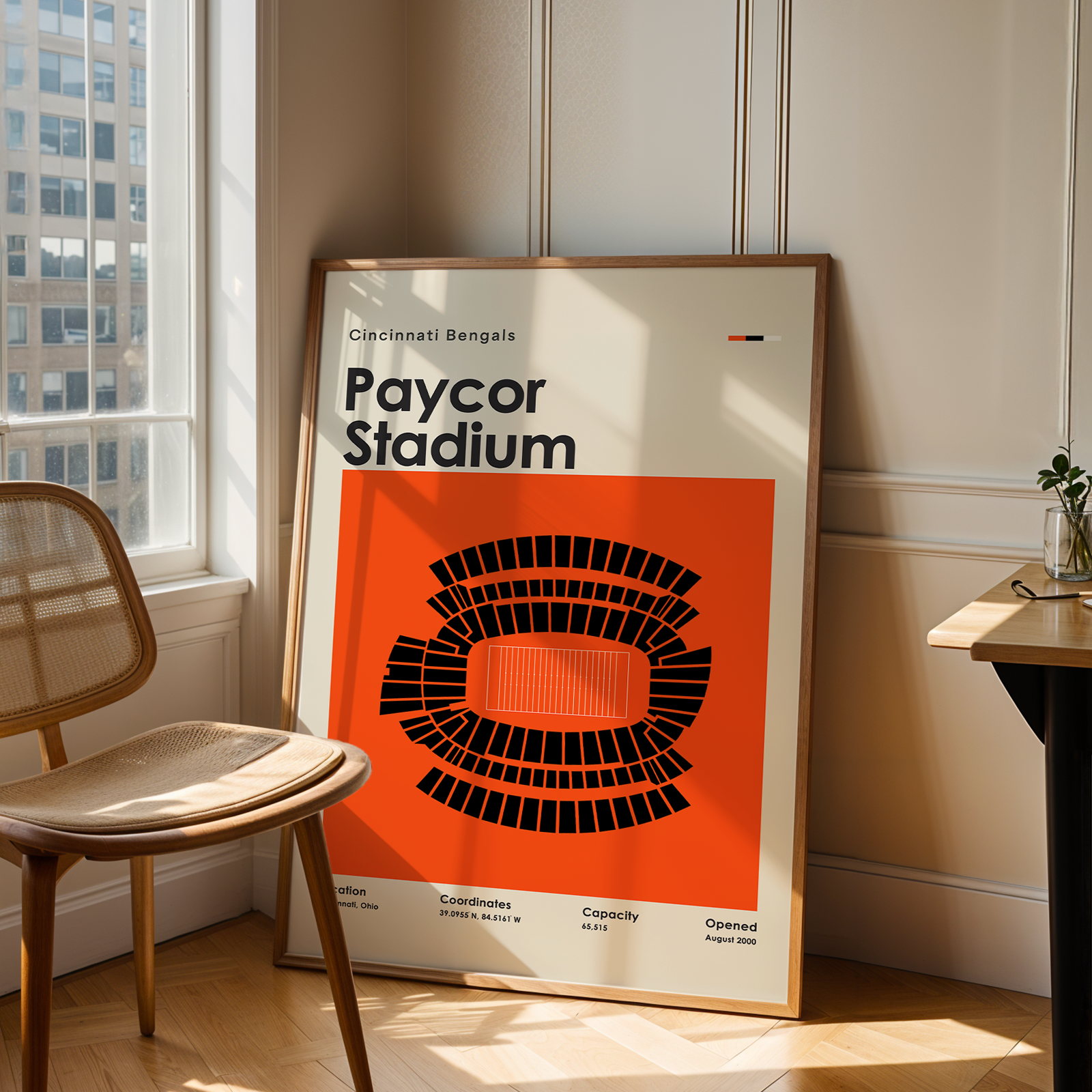 Framed poster of Paycor Stadium in a room with a chair and table.