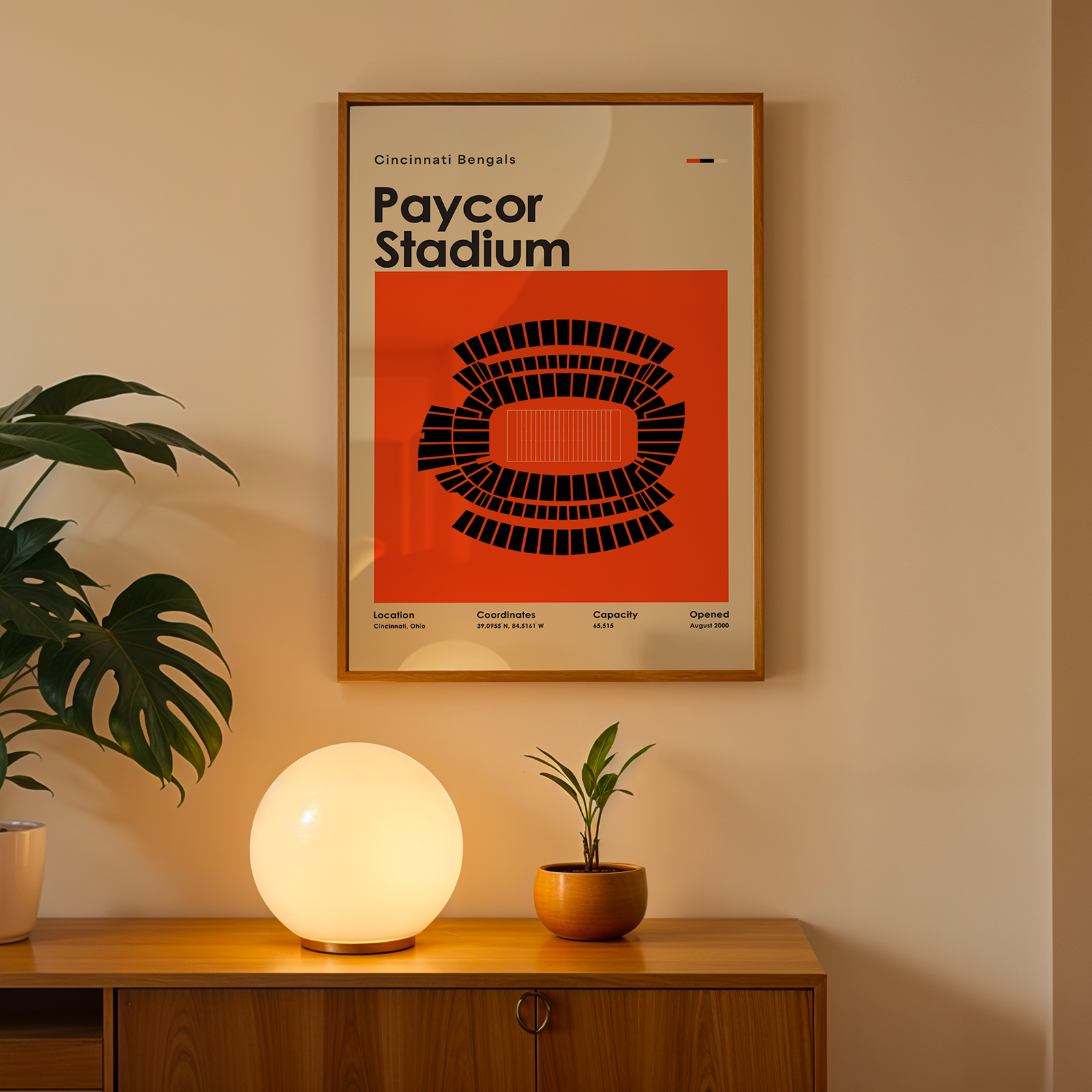 Framed poster of Paycor Stadium on a wall above a wooden cabinet with decorative items.