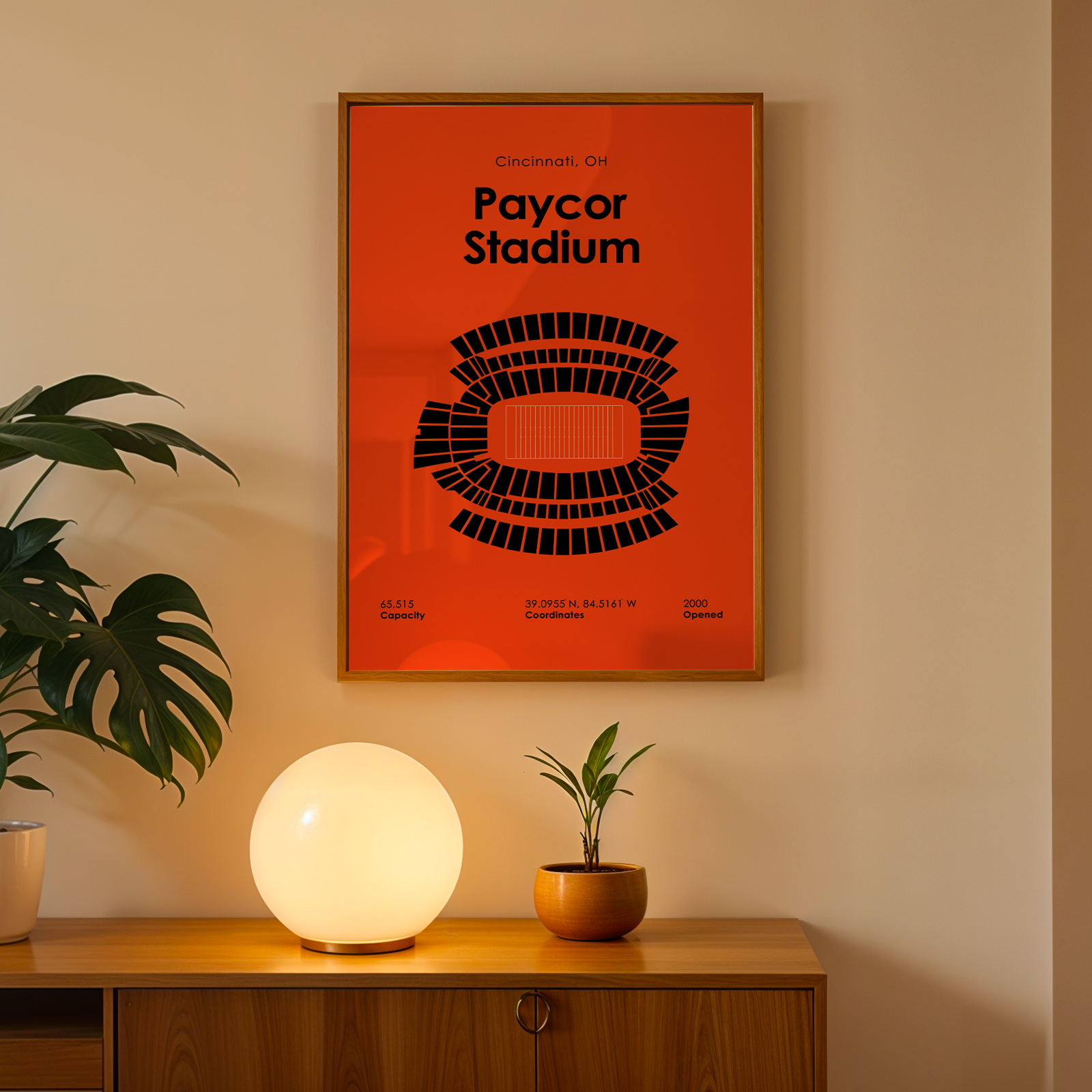 Framed poster of Paycor Stadium on a wall above a wooden cabinet with decorative items.