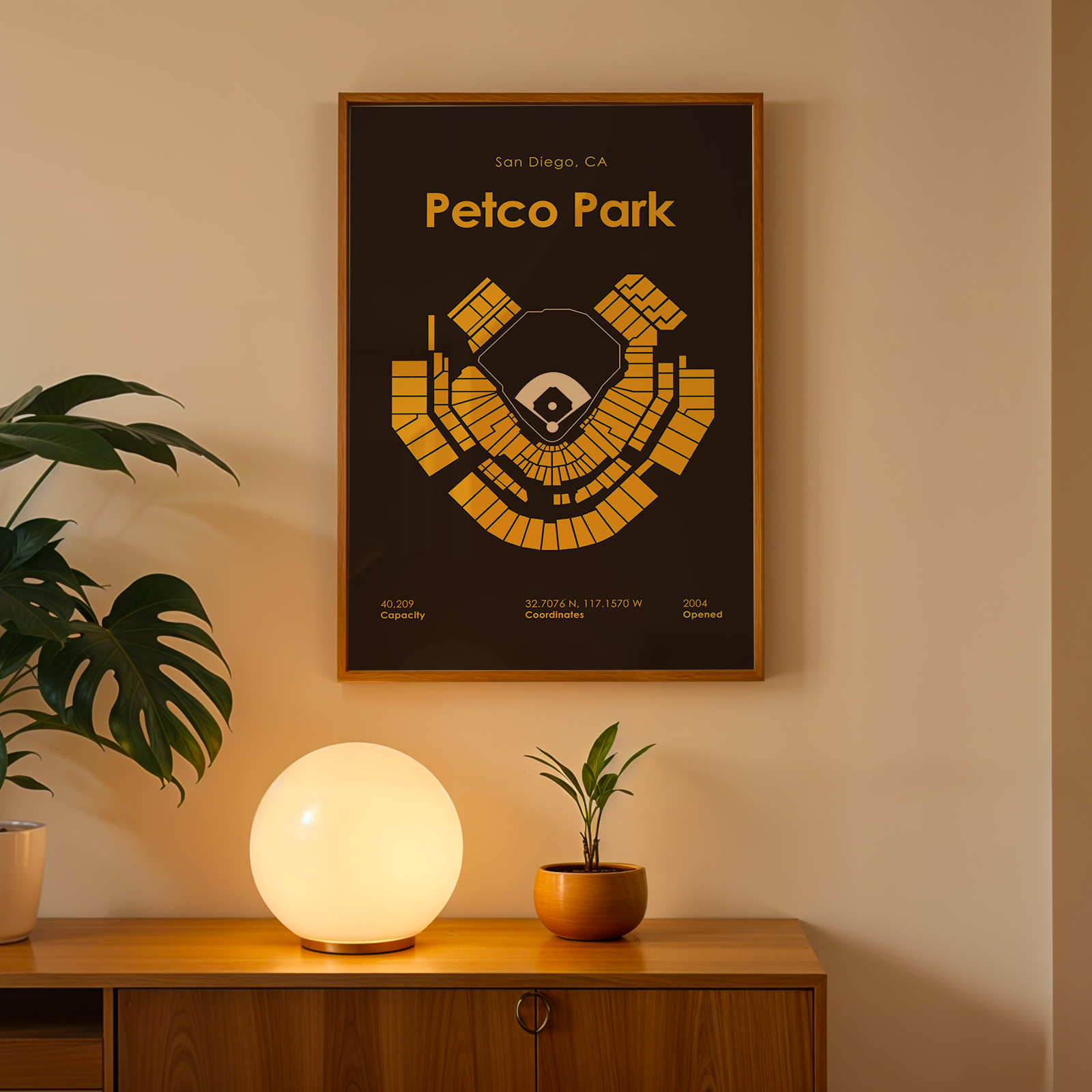 Framed poster of Petco Park on a wall with a lamp and plant below.