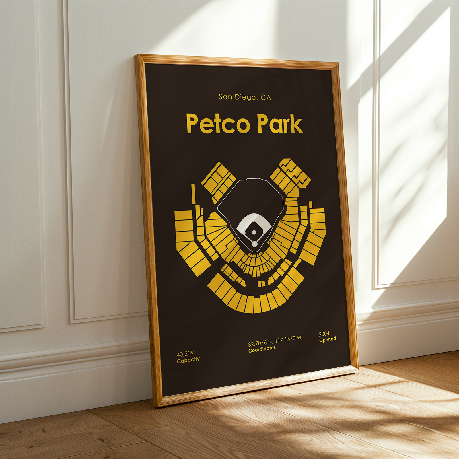 Framed poster of Petco Park layout with yellow design on a black background, leaning against a white wall.