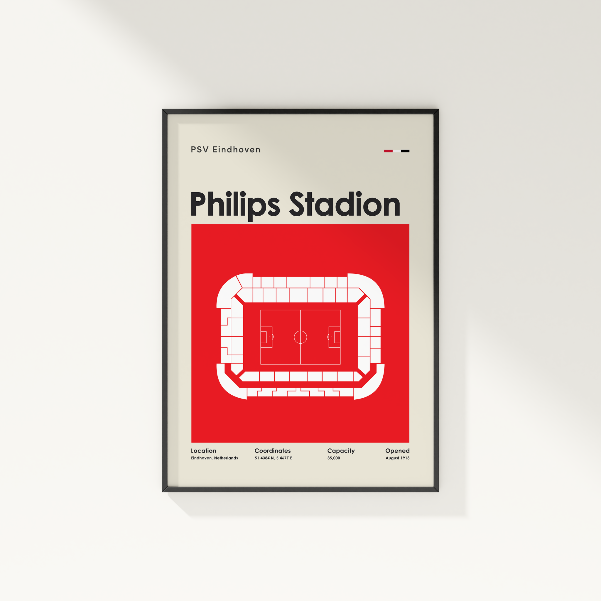 A framed minimalist poster of Philips Stadion in Eindhoven, Netherlands, featuring a red and white stadium floor plan on a light beige background with a thin black frame.