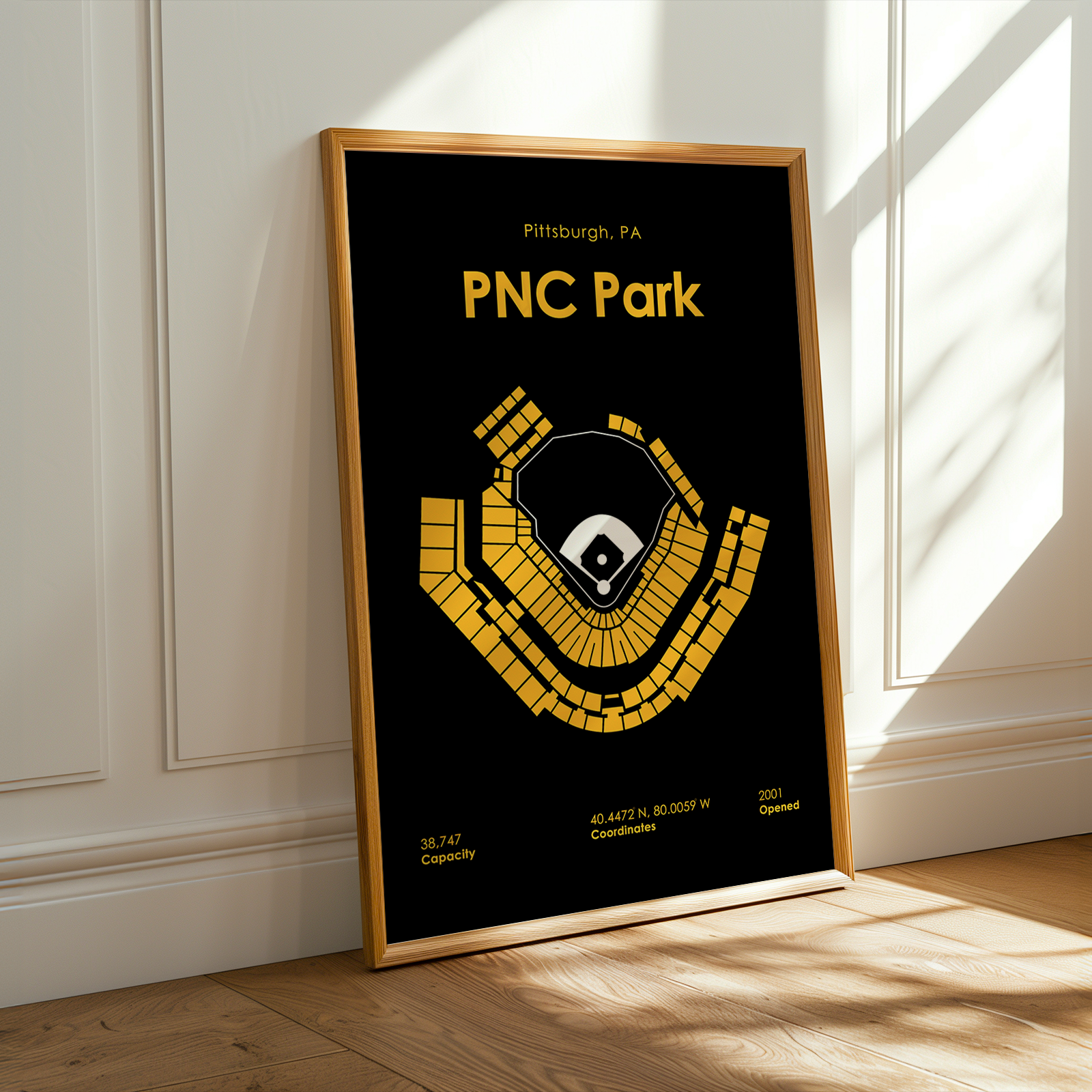 Framed poster of PNC Park with yellow text and design on a black background, leaning against a white wall.