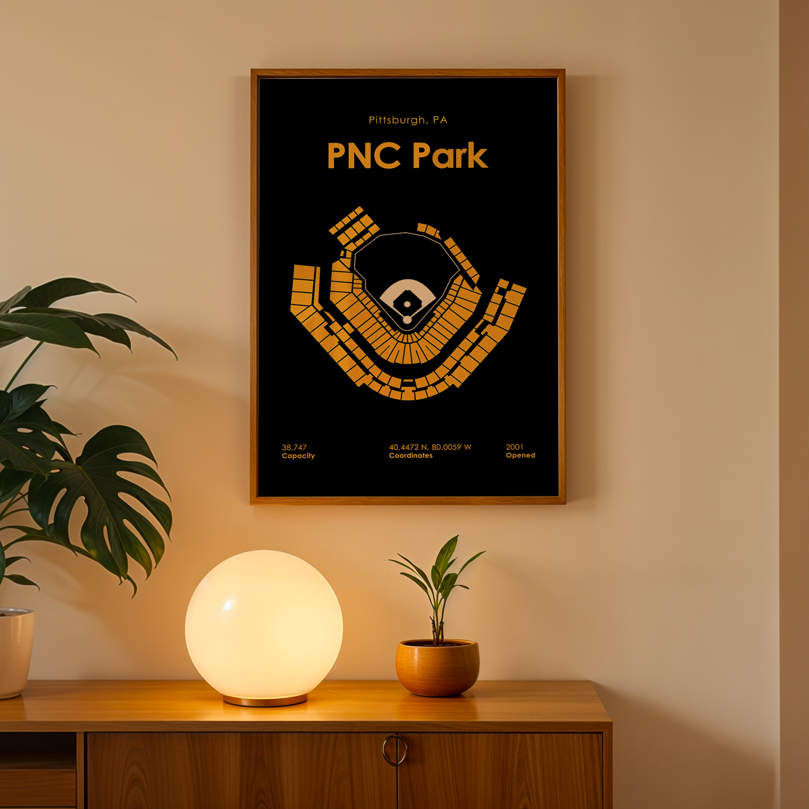 Framed poster of PNC Park with a plant and lamp on a wooden surface.