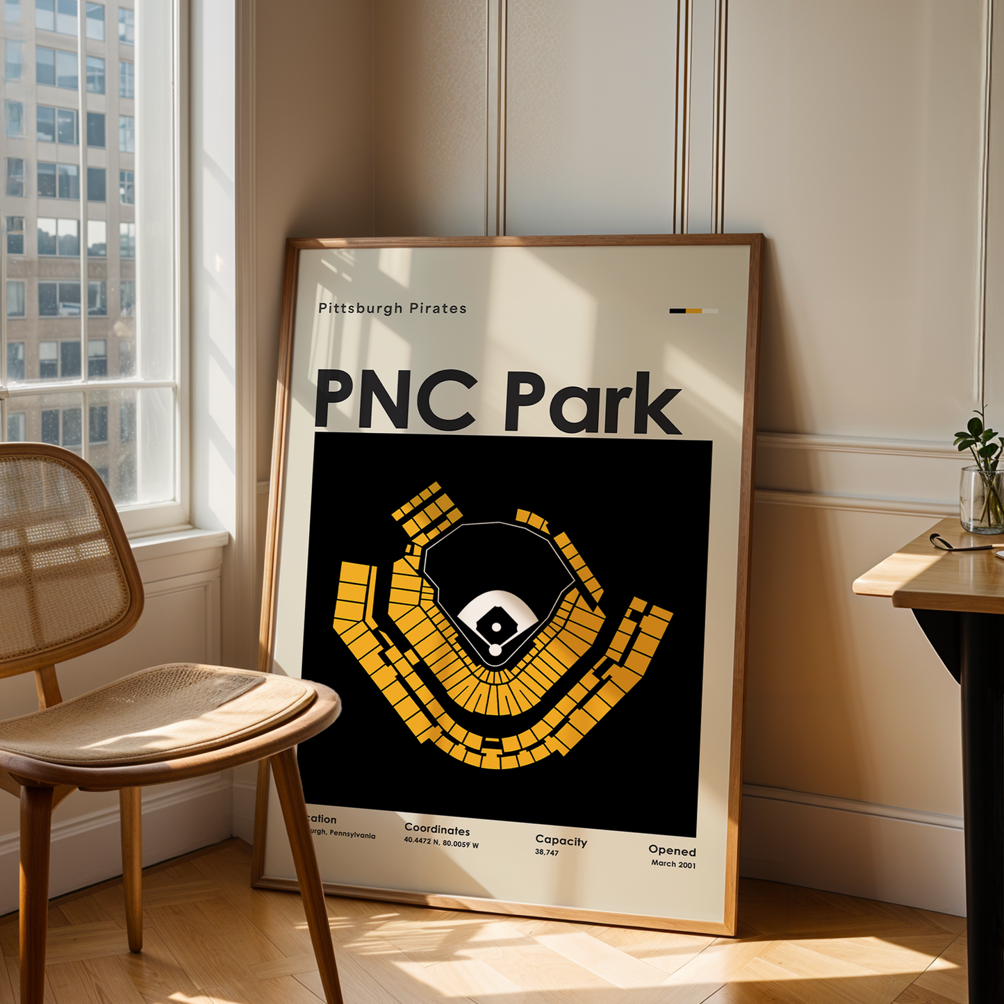 Framed poster of PNC Park in a room with a chair and table.
