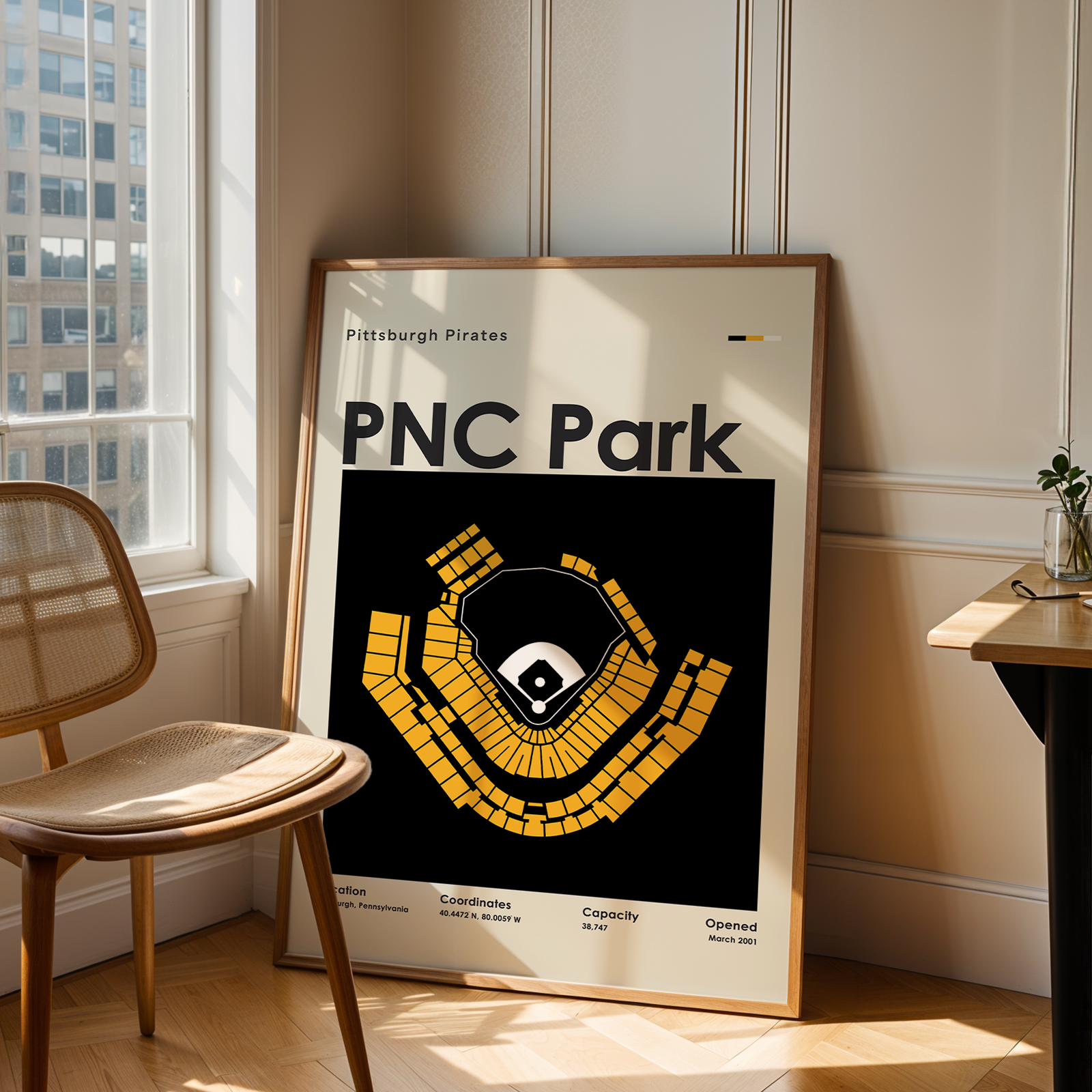 Framed poster of PNC Park in a room with a chair and table.