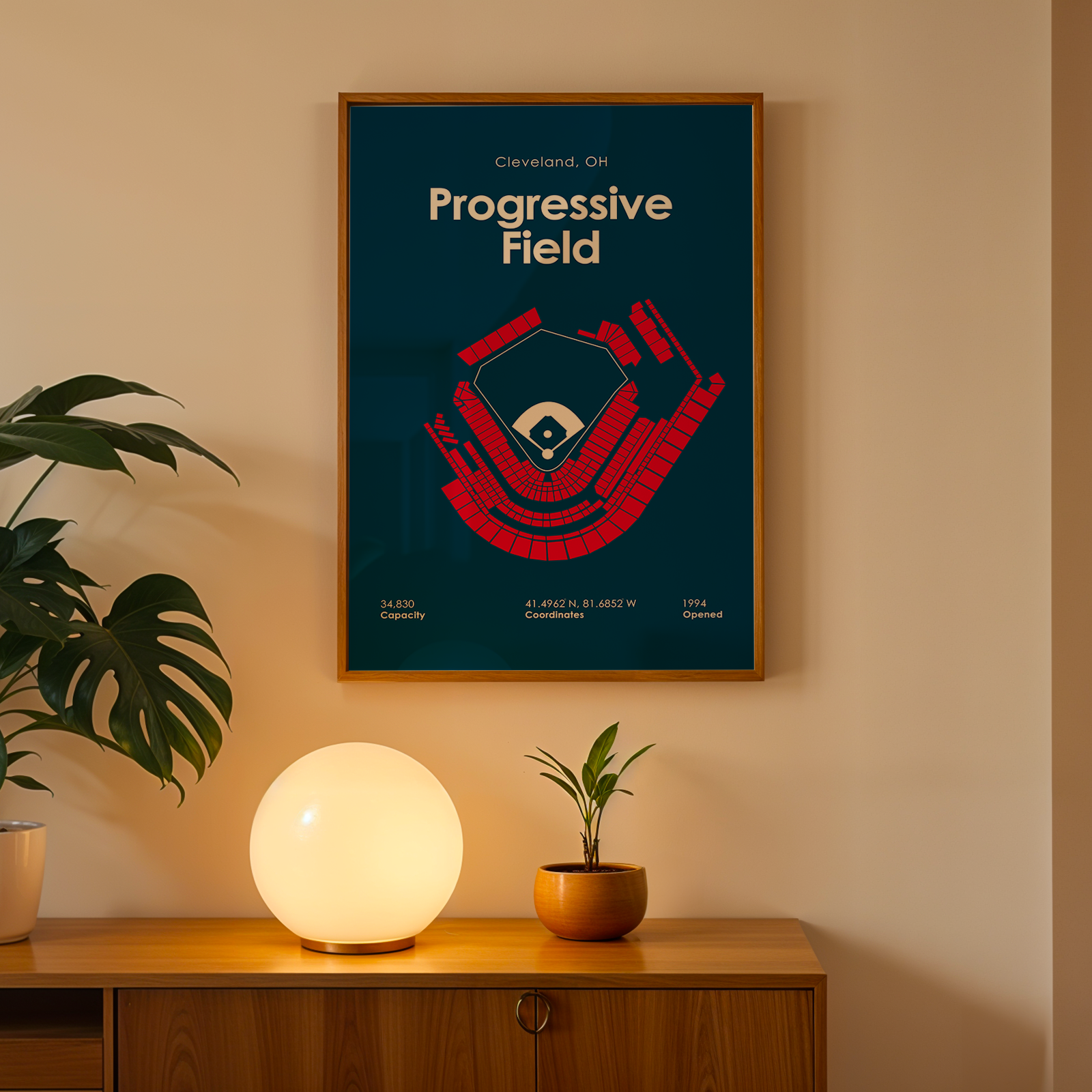 Framed poster of Progressive Field in Cleveland, OH on a wall with a plant and lamp below.