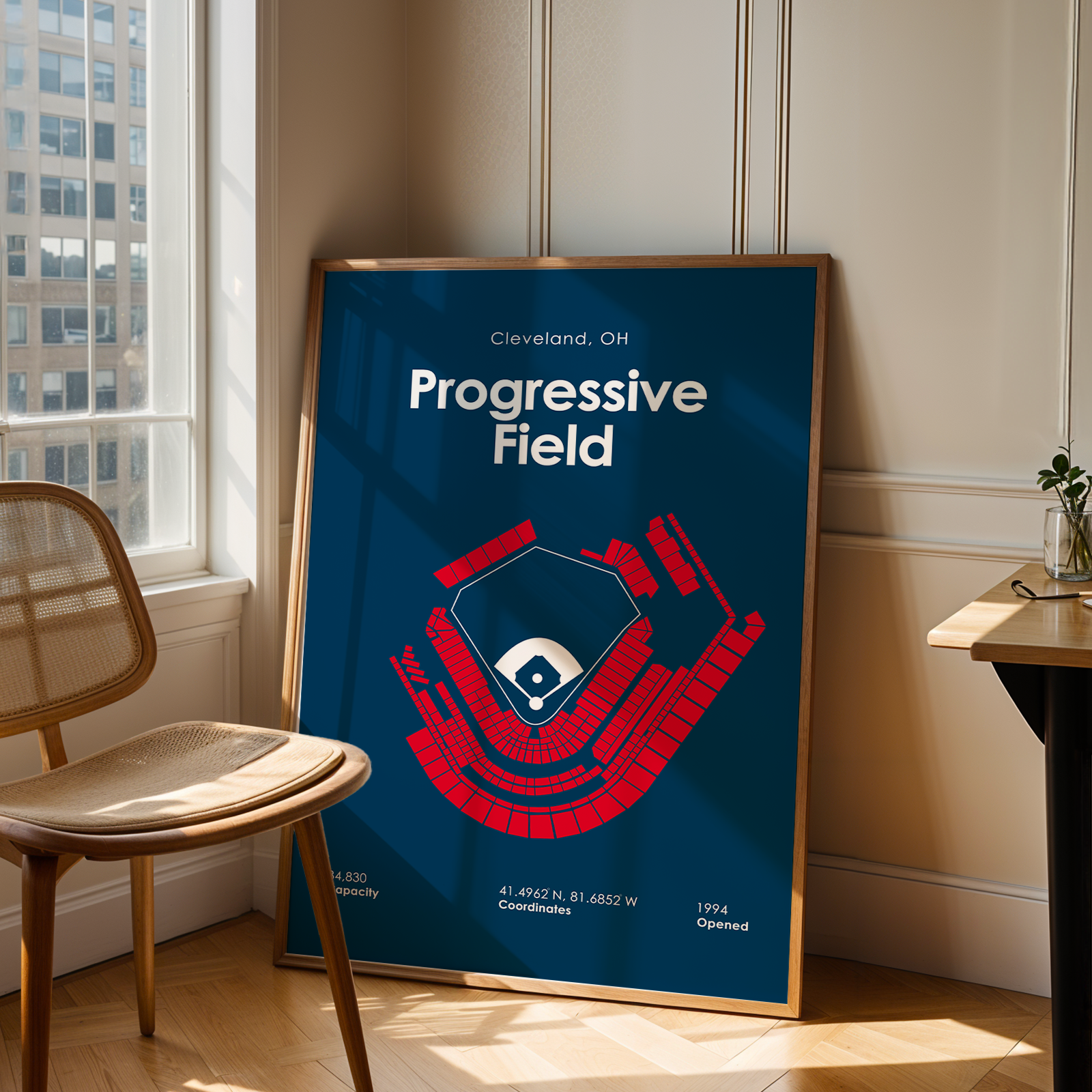 Framed poster of Progressive Field in Cleveland, OH on a wall in a room with a window and chair.