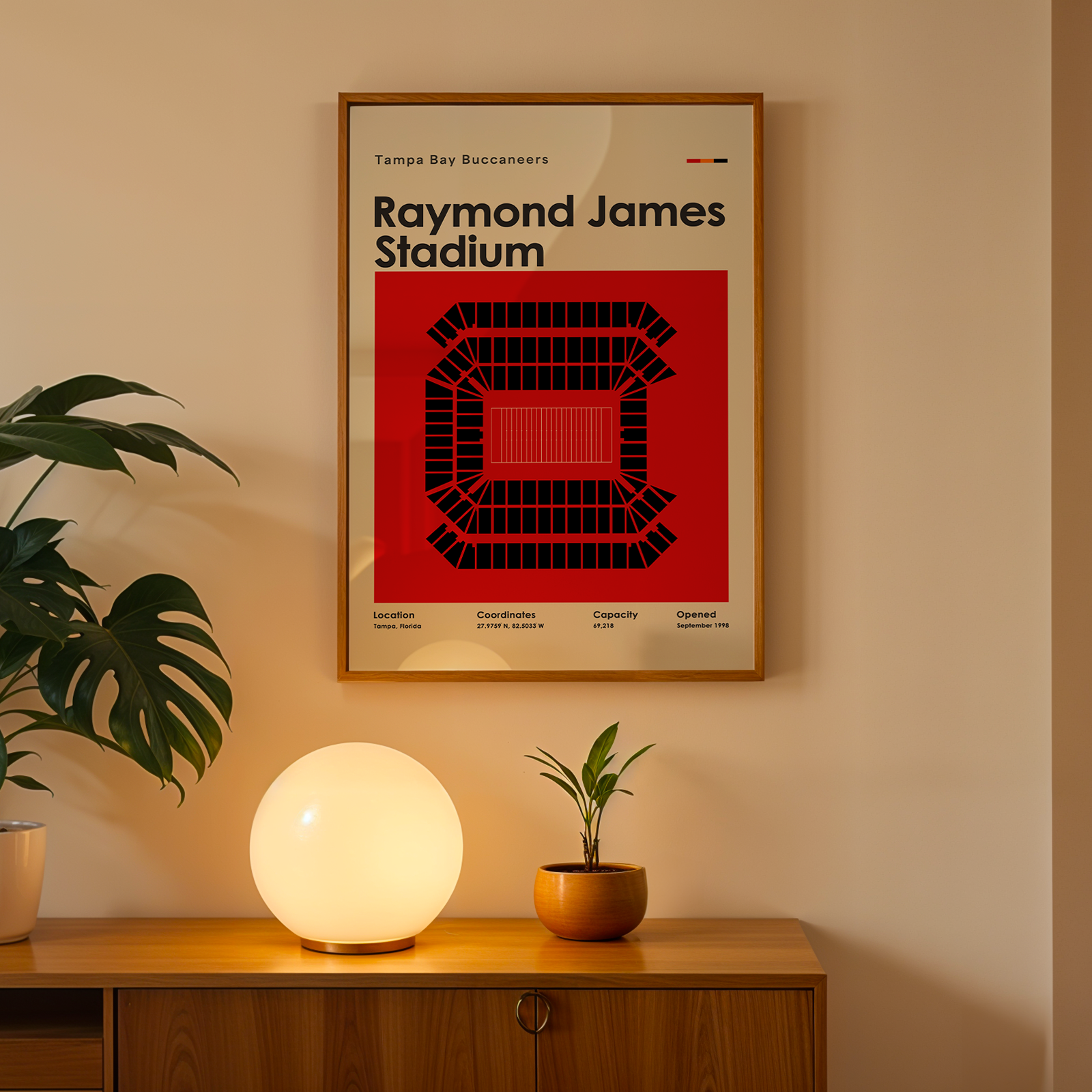 Framed poster of Raymond James Stadium on a wall above a wooden cabinet with decorative items.