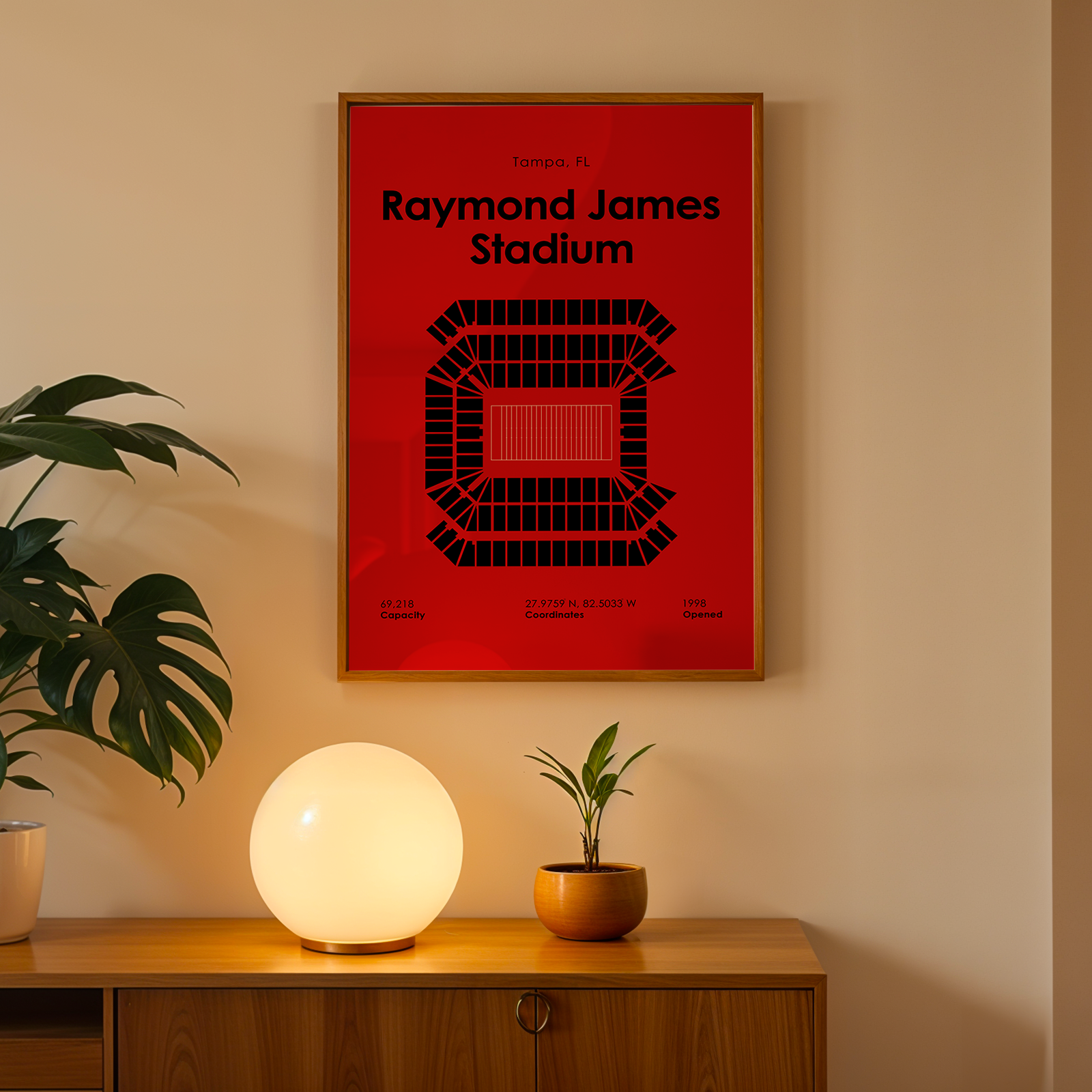 Framed poster of Raymond James Stadium on a wall above a wooden cabinet with decorative items.