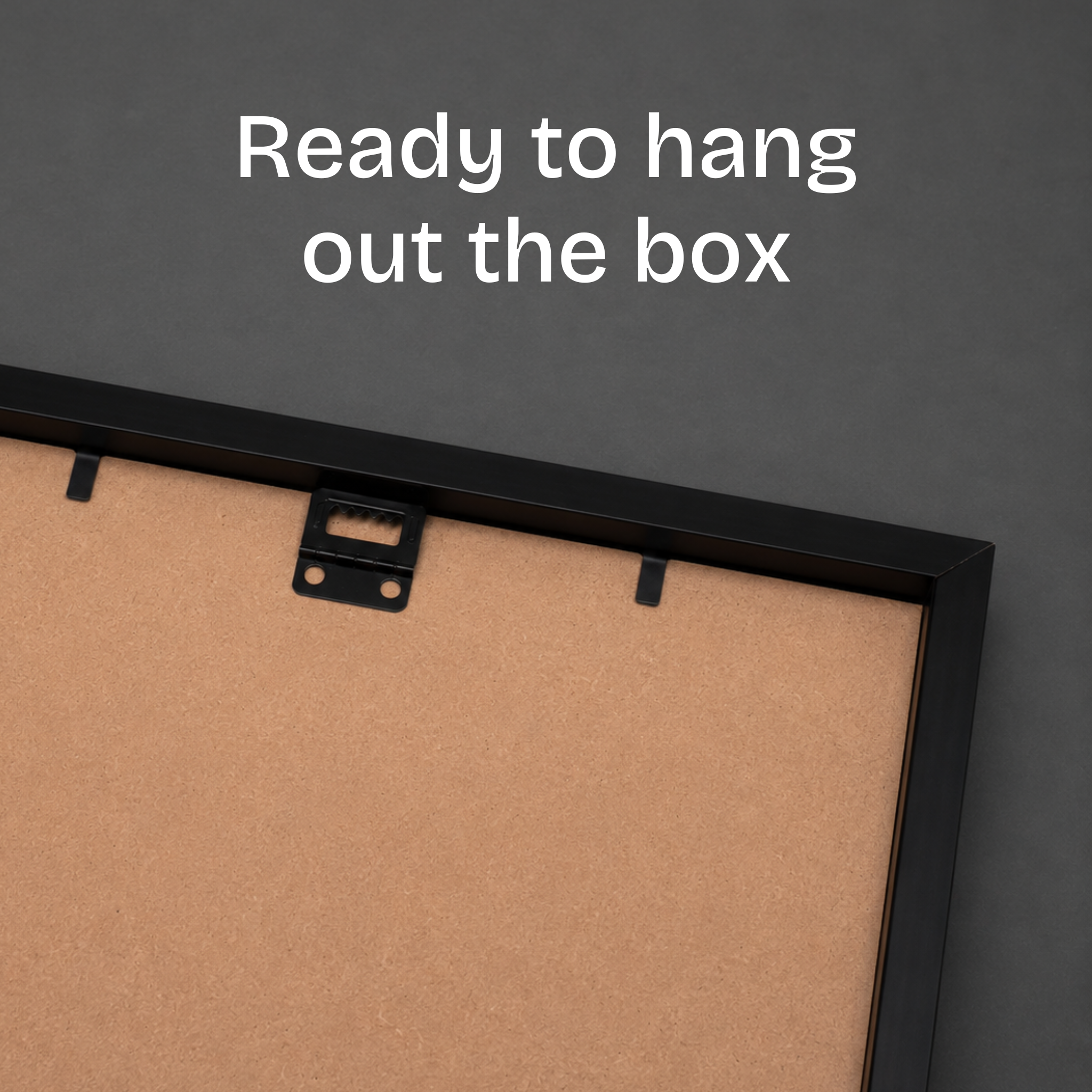 Close-up of the back of a picture frame with a black frame and tan cork backing, with white text reading 'Ready to hang out the box' on a dark gray background.