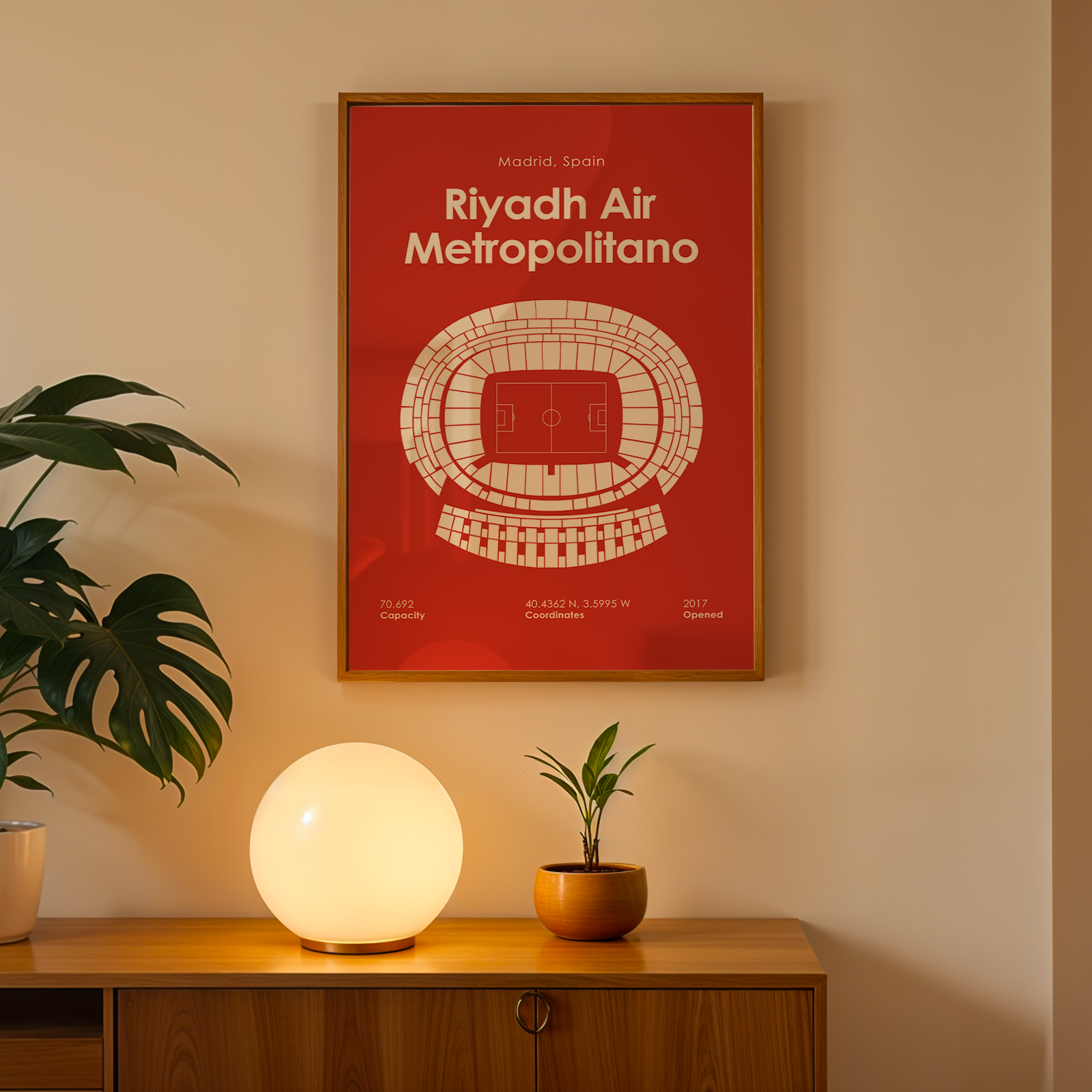 Framed poster of Riyadh Air Metropolitano on a wall with a lamp and plant below.