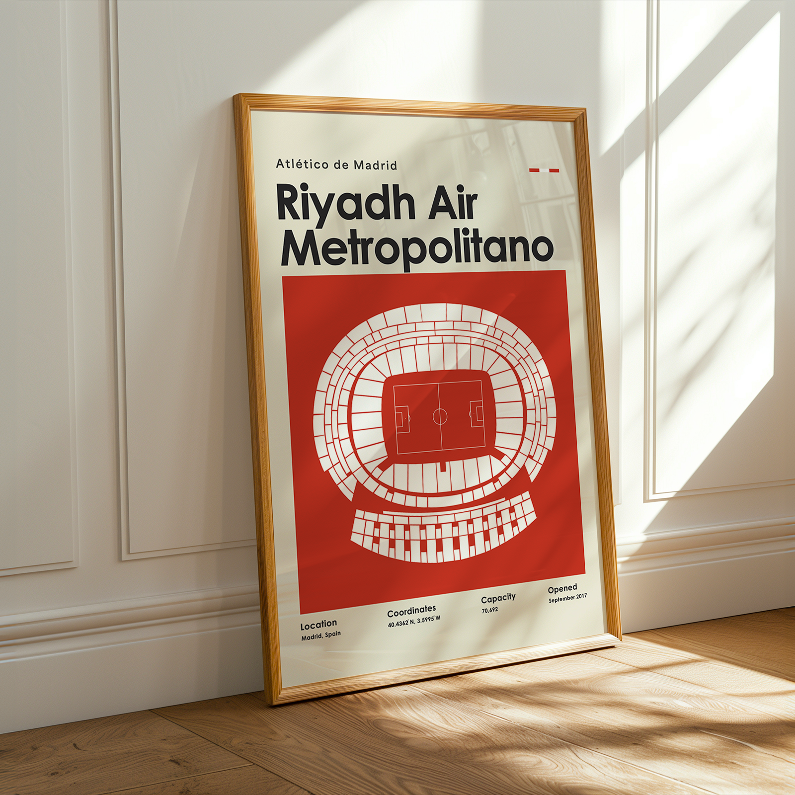 Framed poster of Riyadh Air Metropolitano stadium layout on a wooden floor with sunlight streaming through a window.