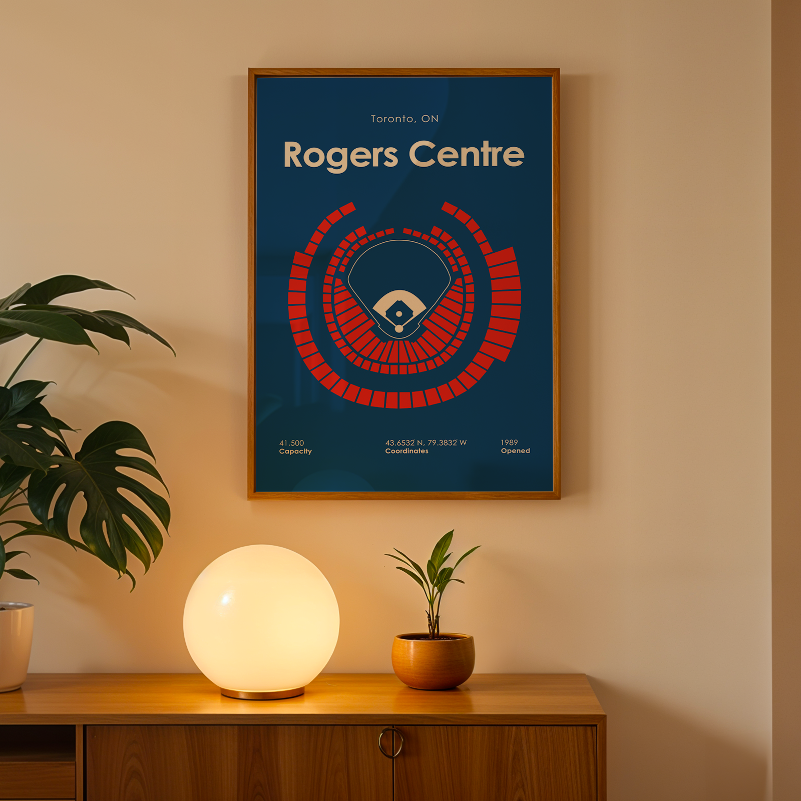 Framed poster of Rogers Centre on a wall with a plant and lamp below.