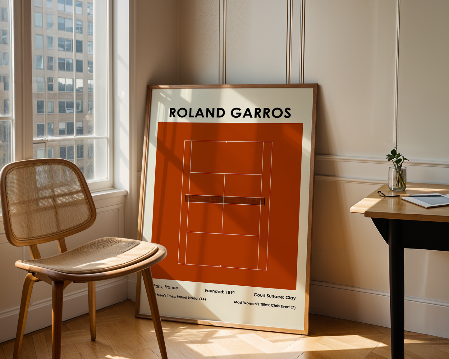 Framed poster of Roland Garros tennis court design in a room with a chair and table.