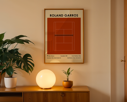 Framed poster of Roland Garros tennis court on a wall with a wooden cabinet and plants below.