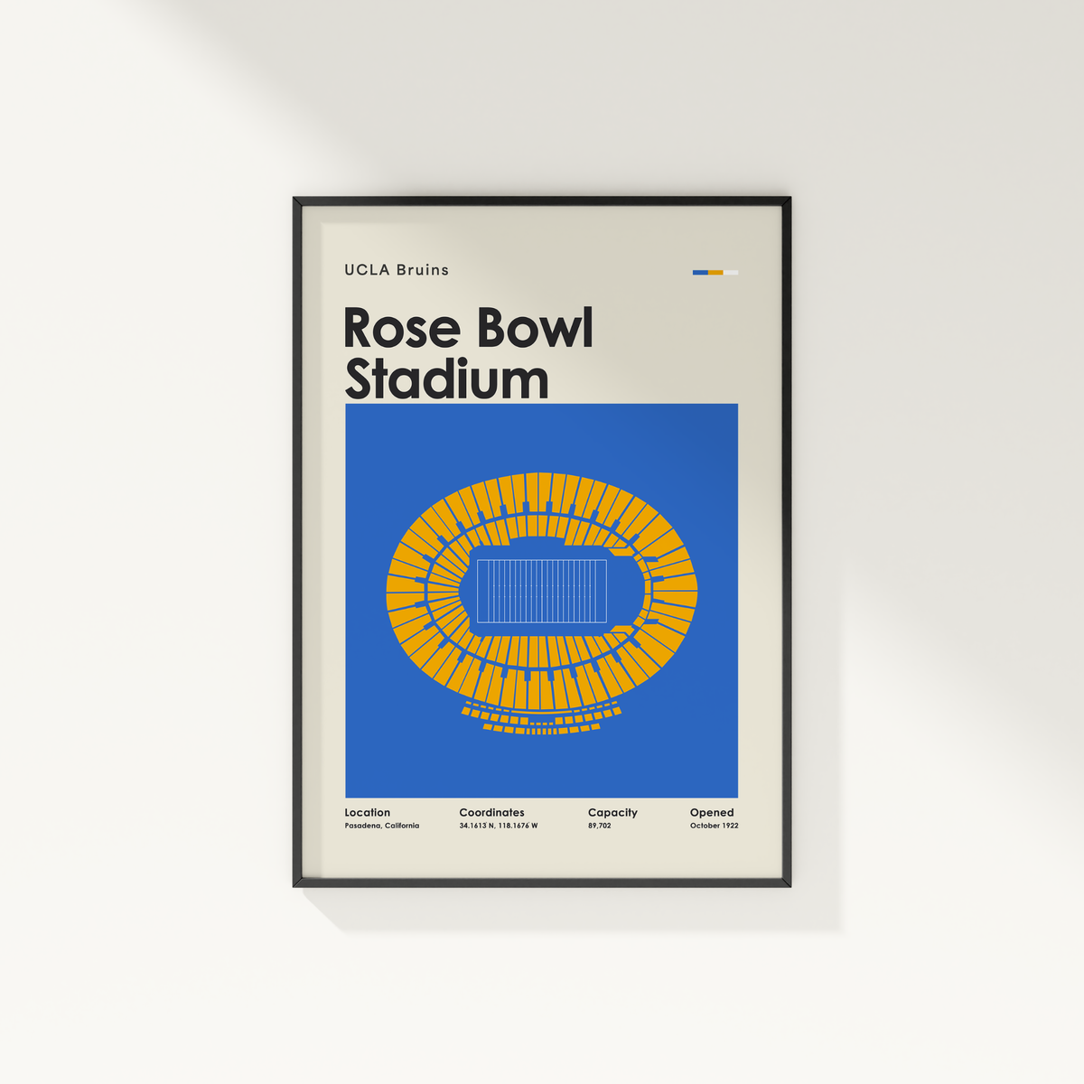 A framed poster of UCLA Bruins Rose Bowl Stadium featuring a blue background with a yellow stadium graphic, mounted on a light gray wall.