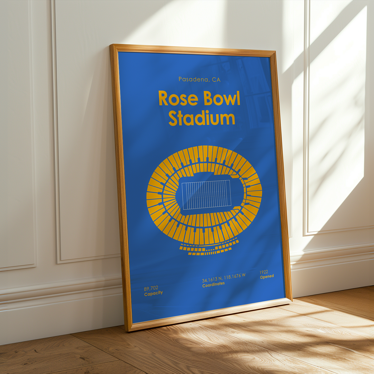 A framed poster of Rose Bowl Stadium leaning against a white paneled wall on a wooden floor, with warm sunlight casting shadows across the scene.