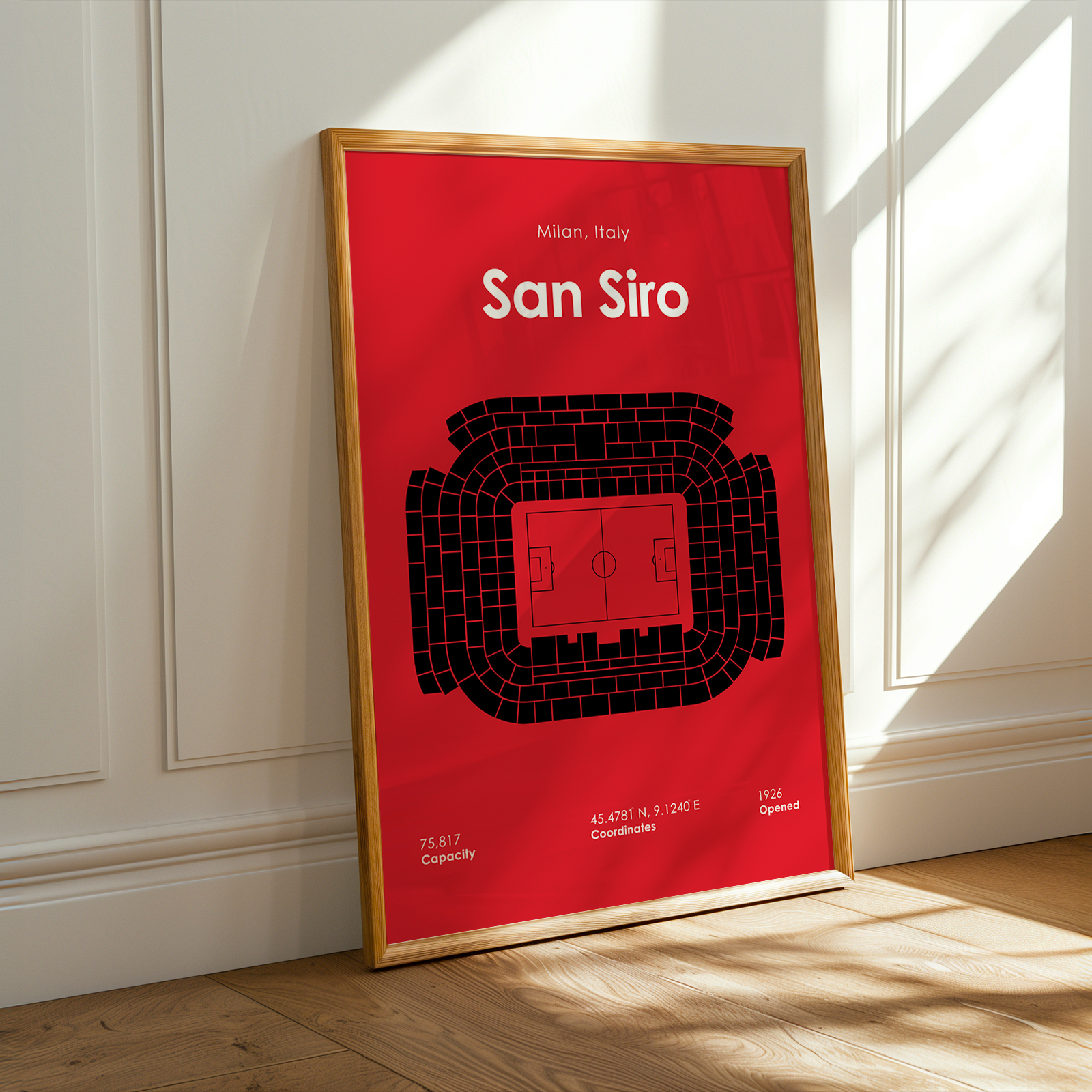 Framed poster of San Siro stadium layout on a red background, leaning against a white wall.