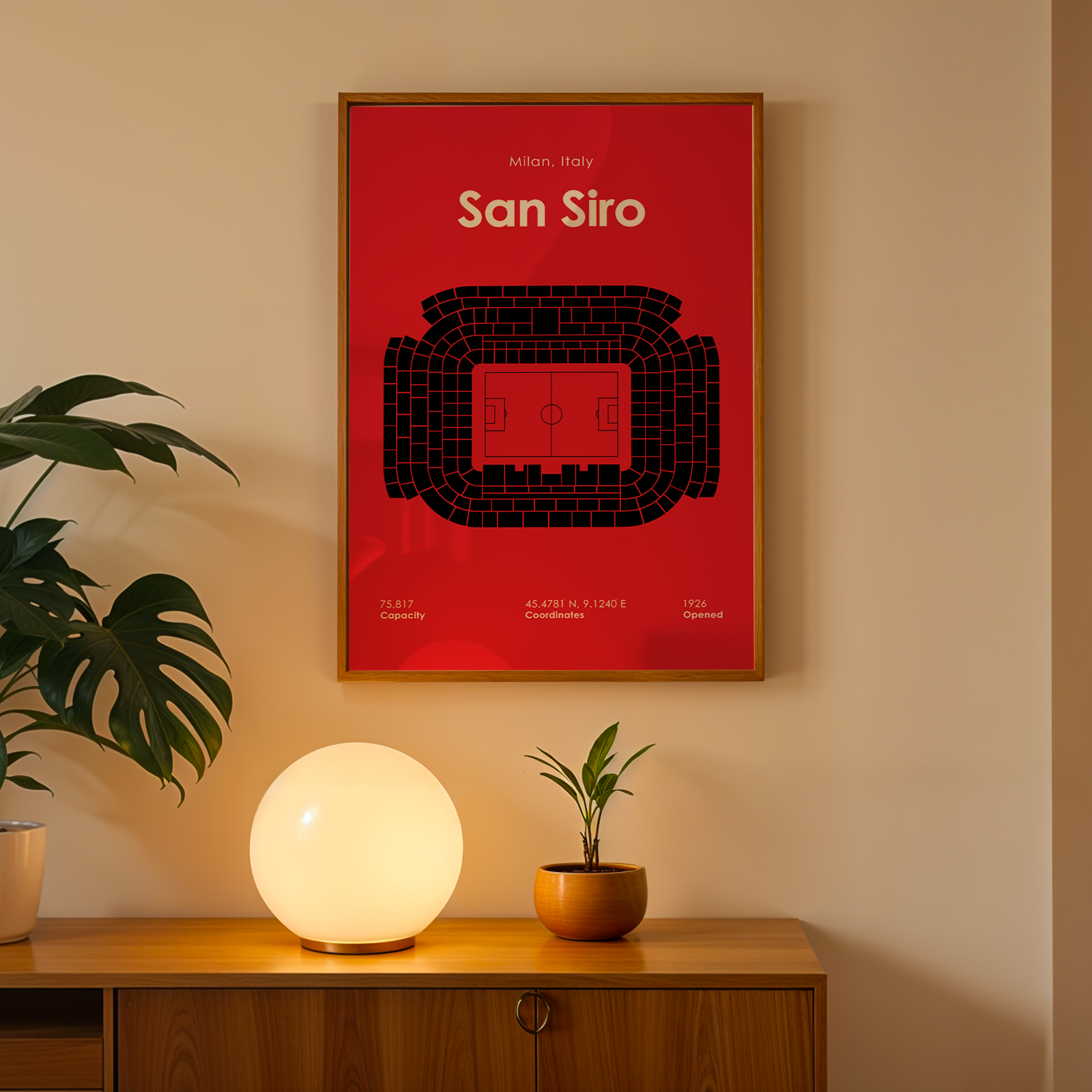Framed poster of San Siro stadium on a wall with a lamp and plant below.