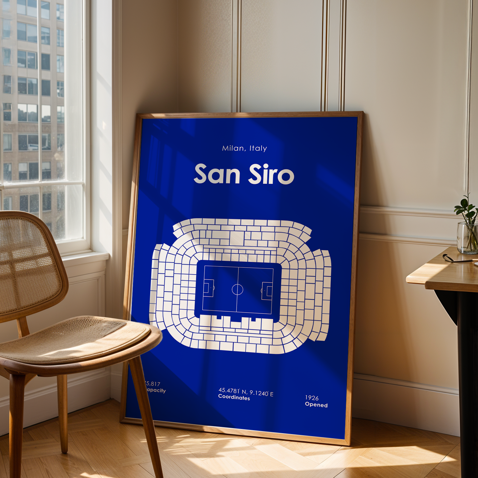 Framed poster of San Siro stadium layout in a room with a chair and window.