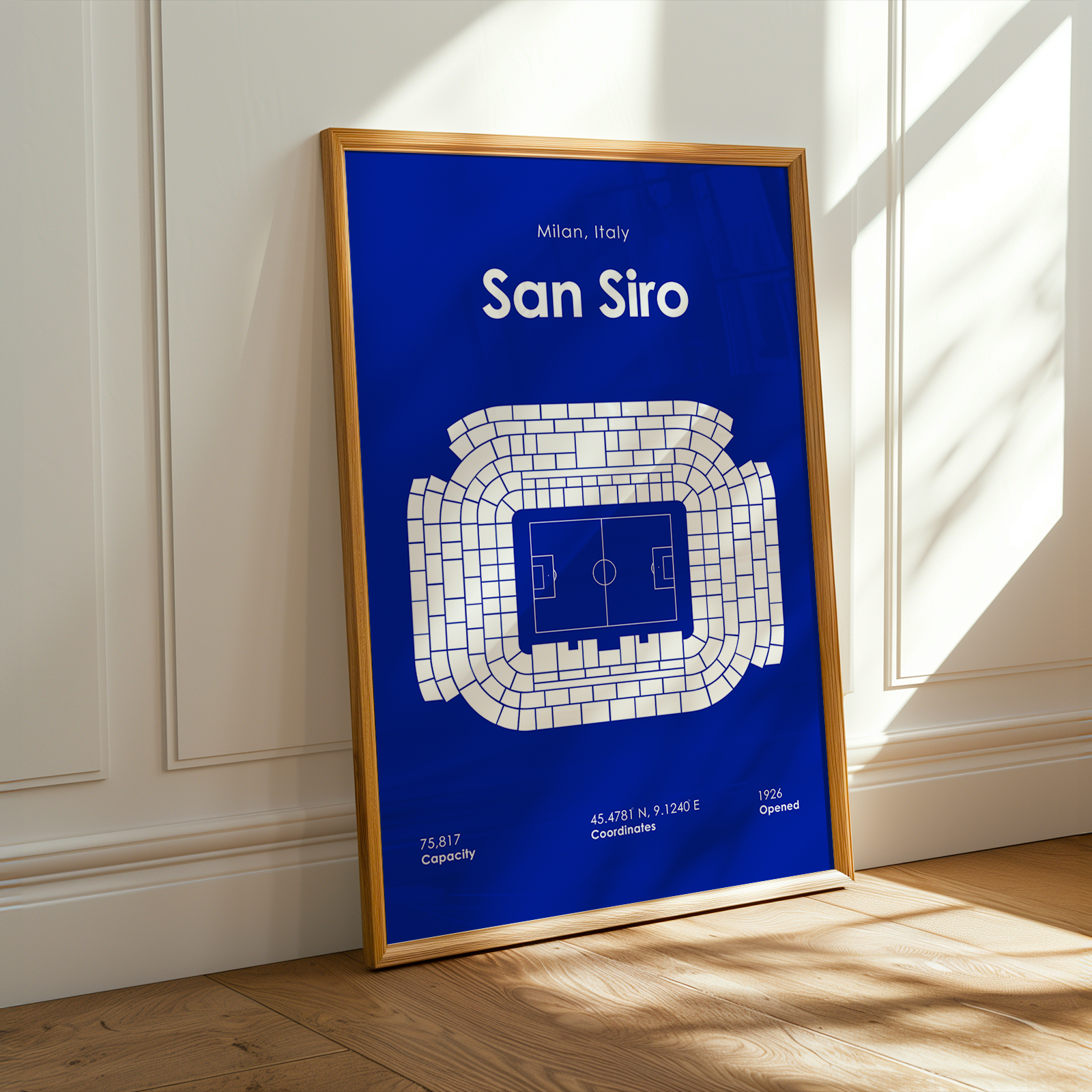 Framed poster of San Siro stadium layout on a blue background, leaning against a white wall.