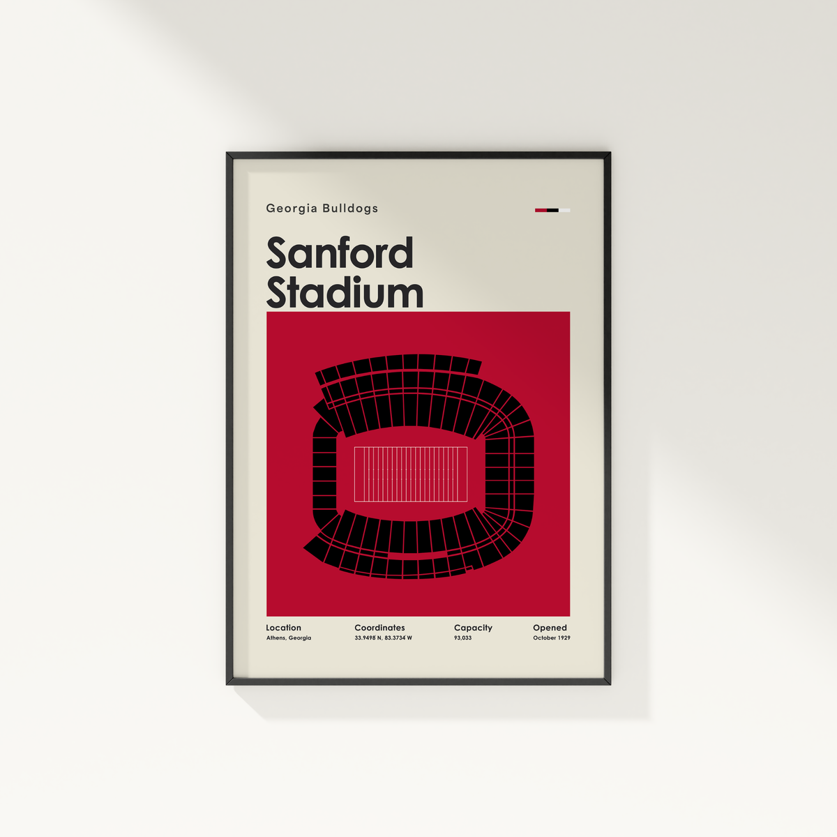 A framed minimalist poster of Sanford Stadium from the Georgia Bulldogs, featuring a bold red and black stadium graphic on a cream background, shown hanging on a light gray wall.