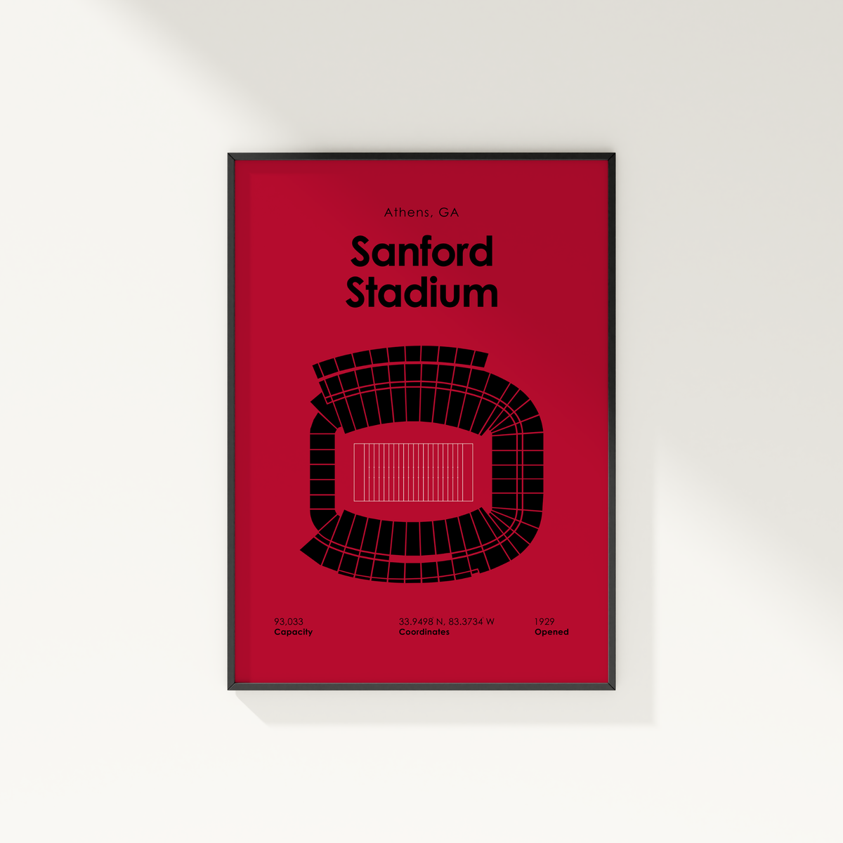 A framed minimalist poster of Sanford Stadium in Athens, GA, featuring a bold red background with black text and a black stadium outline illustration, mounted on a light gray wall.