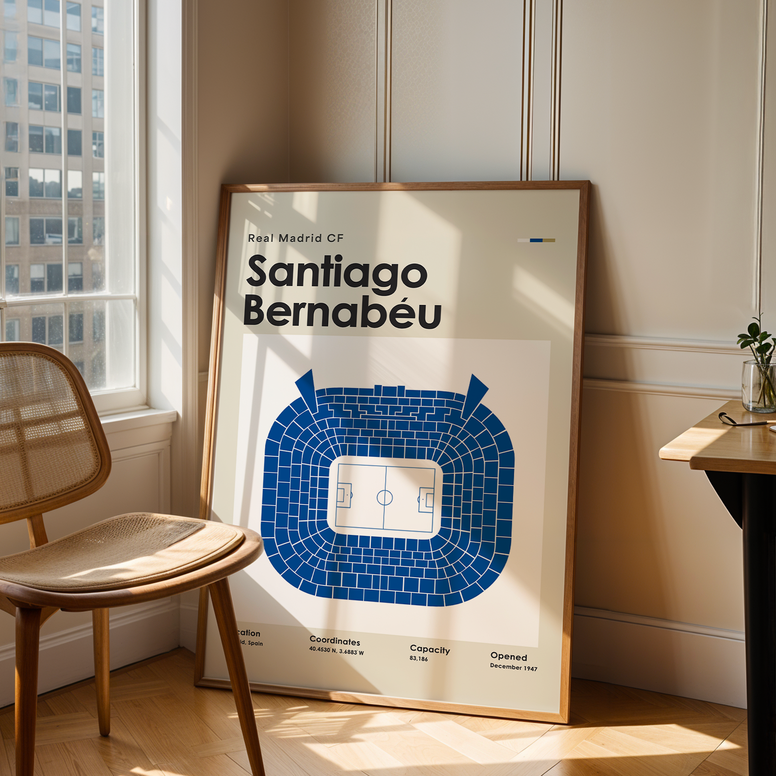 Framed poster of Santiago Bernabéu stadium in a room with a chair and table.