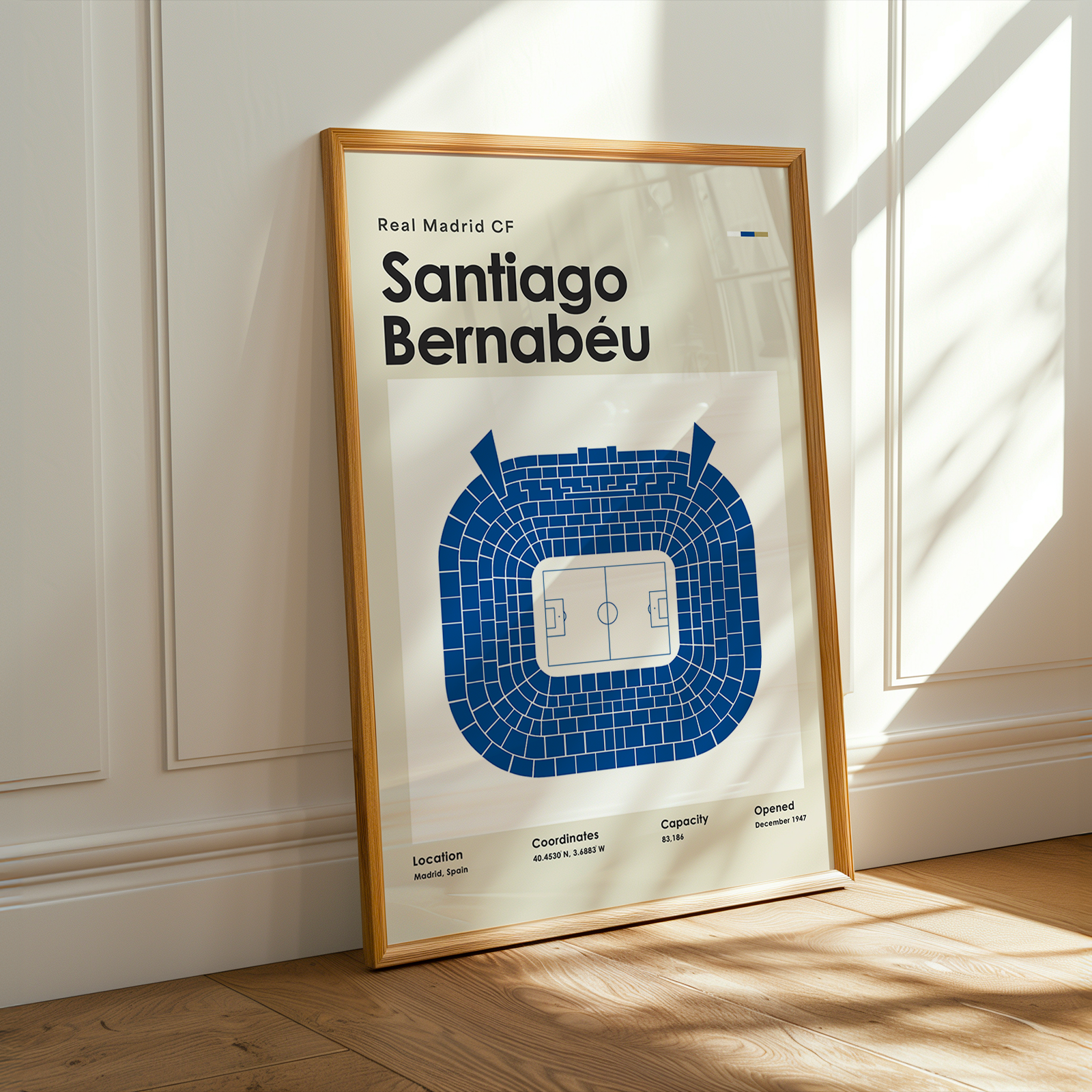 Framed poster of Santiago Bernabeu stadium layout on a wooden floor with sunlight streaming through a window.