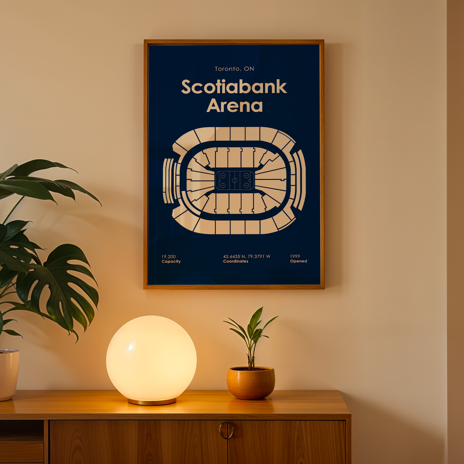 Framed poster of Scotiabank Arena on a wall with a plant and lamp below.