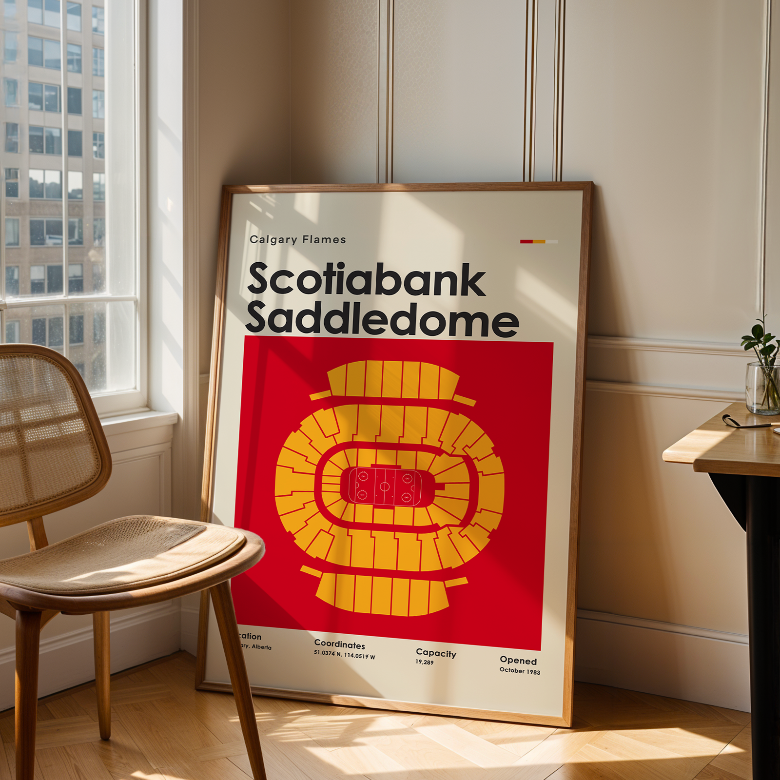 Framed poster of Scotiabank Saddledome in a room with a chair and table.