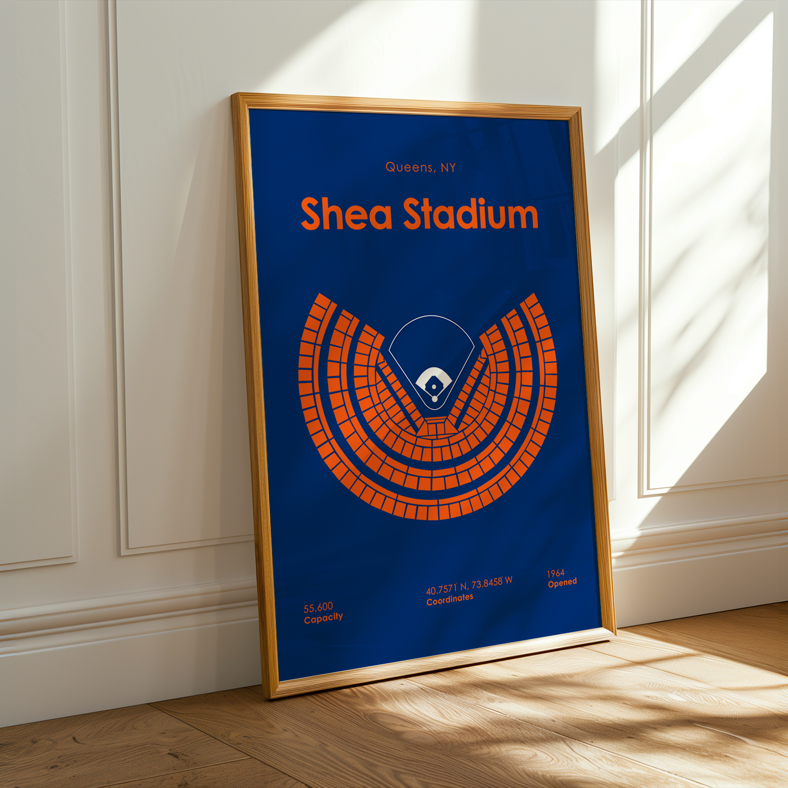 Framed poster of Shea Stadium with a blue background and orange seating diagram, leaning against a white wall.