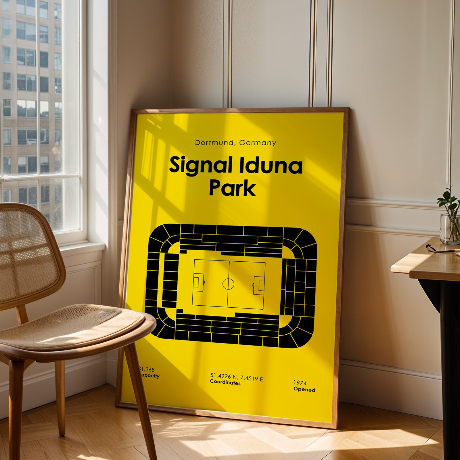 Framed poster of Signal Iduna Park in Dortmund, Germany, leaning against a wall in a room with a chair and table.