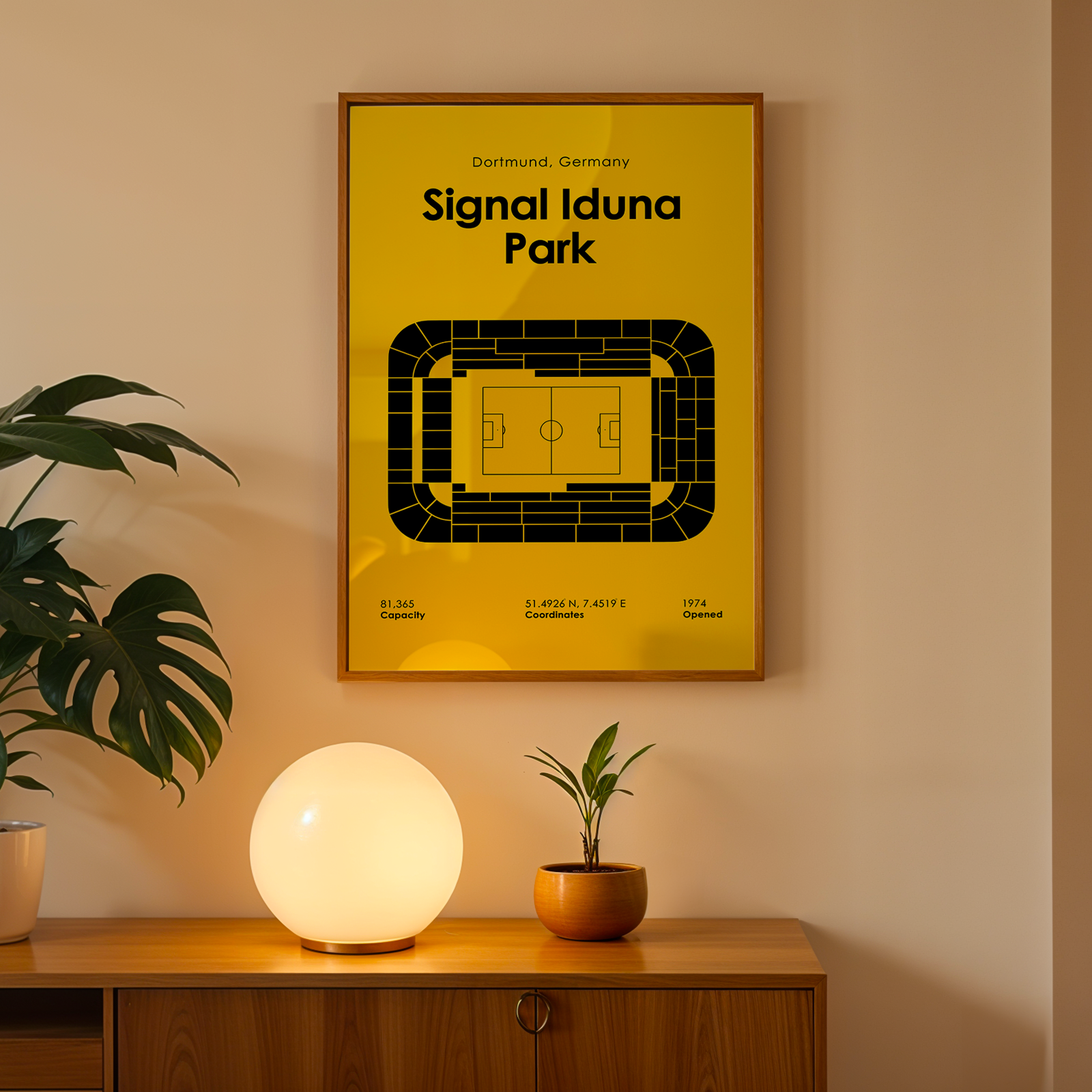 Framed poster of Signal Iduna Park on a wall with a lamp and plant below.