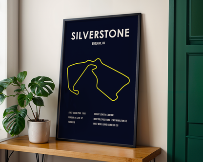 Framed poster of Silverstone circuit layout on a wall with a plant and wooden shelf.