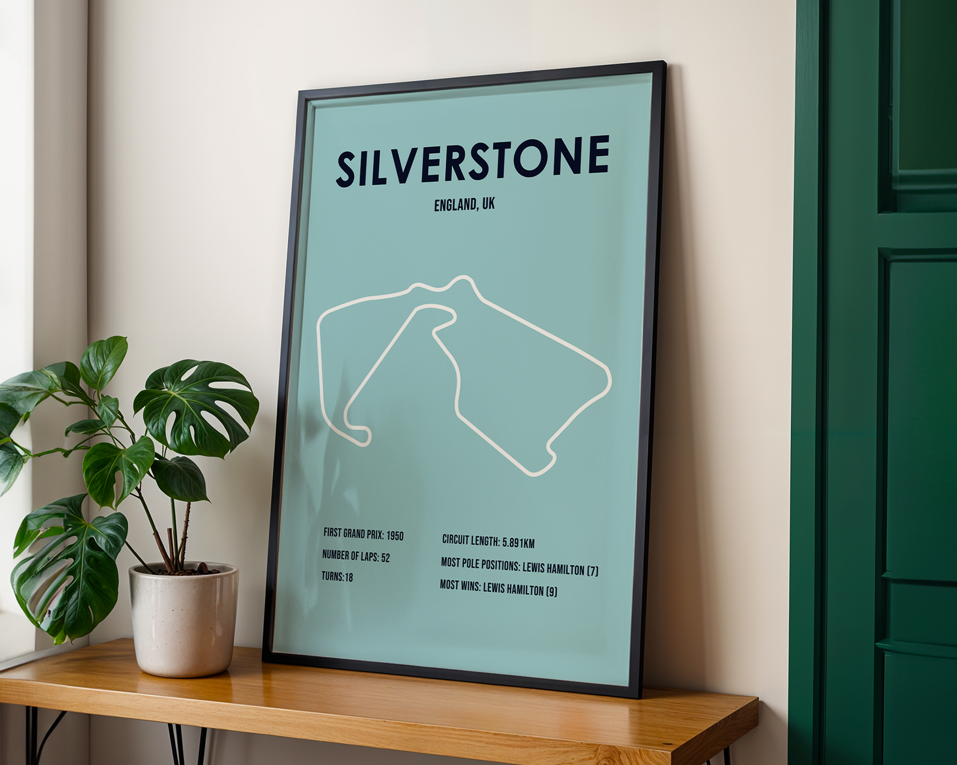 Framed poster of Silverstone circuit layout on a wall with a plant and wooden shelf.