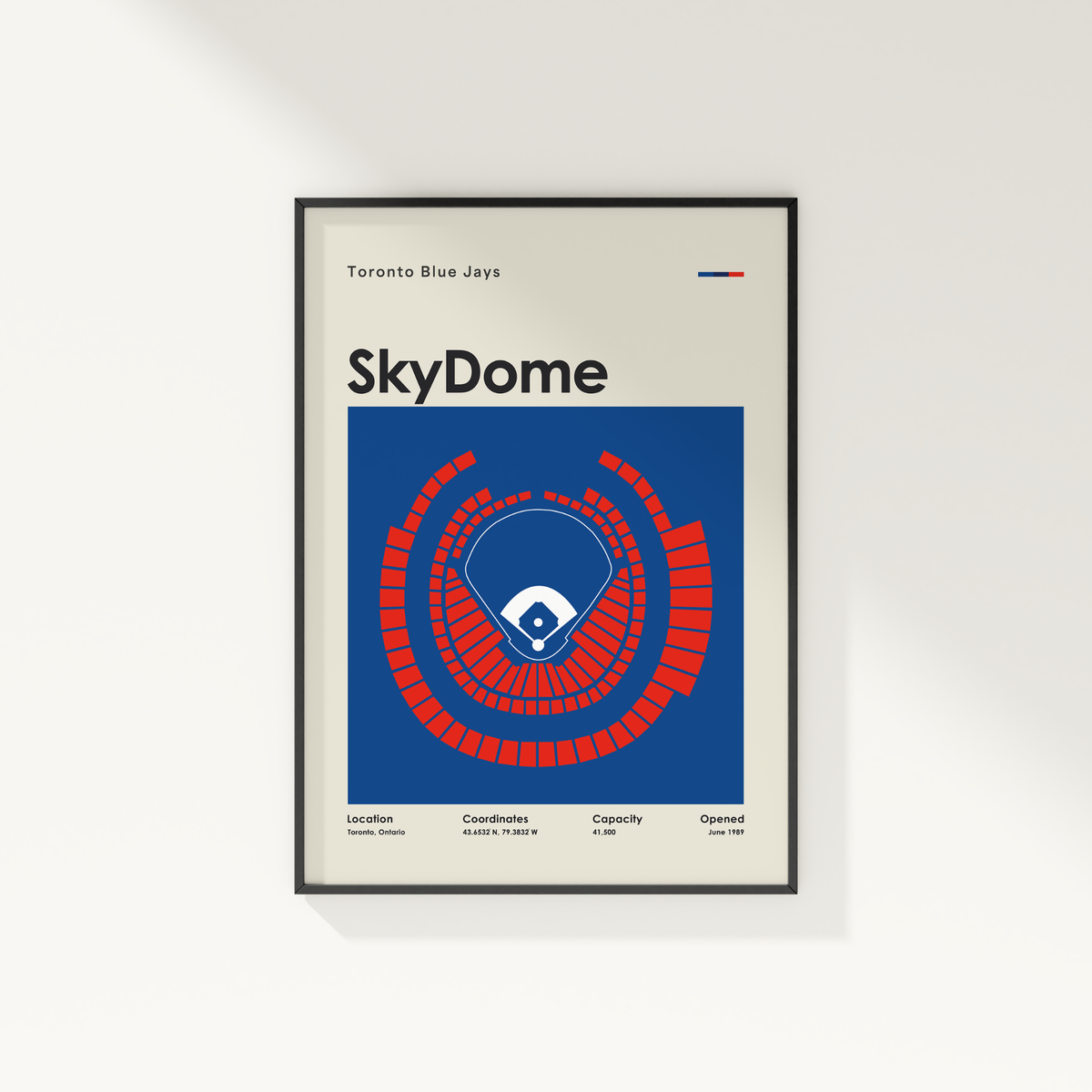A framed Toronto Blue Jays SkyDome sports poster on a clean white wall. The poster features a blue and red stadium layout graphic with team text at the top and bottom, enclosed in a thin black frame.