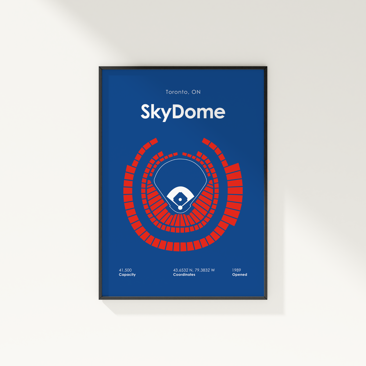 A framed poster featuring a blue stadium layout with a red circular seating arrangement and the text 'Toronto, ON SkyDome' on a white wall.