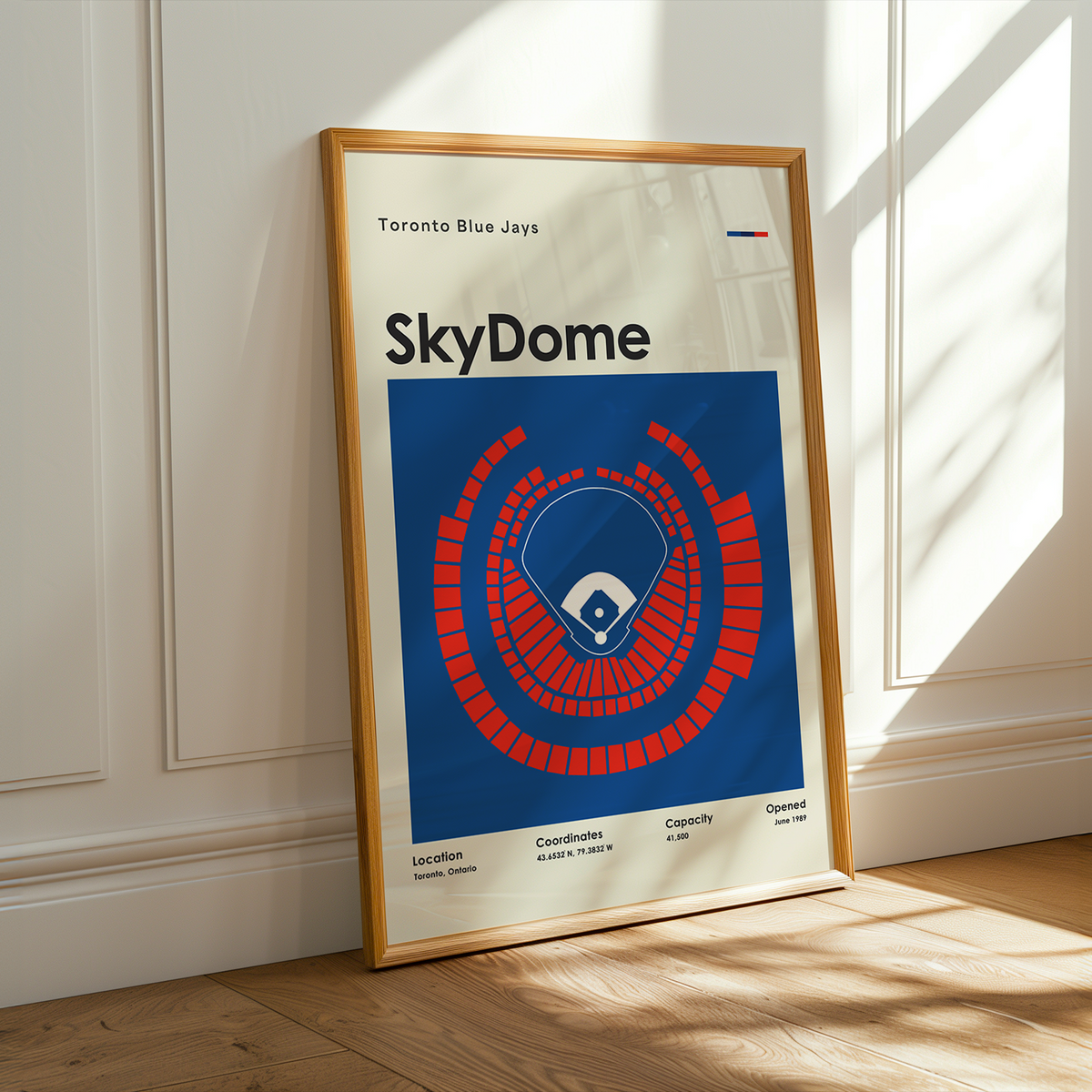 A framed Toronto Blue Jays 'SkyDome' poster leaning against a white paneled wall on a light wood floor, with warm sunlight casting shadows across the scene.