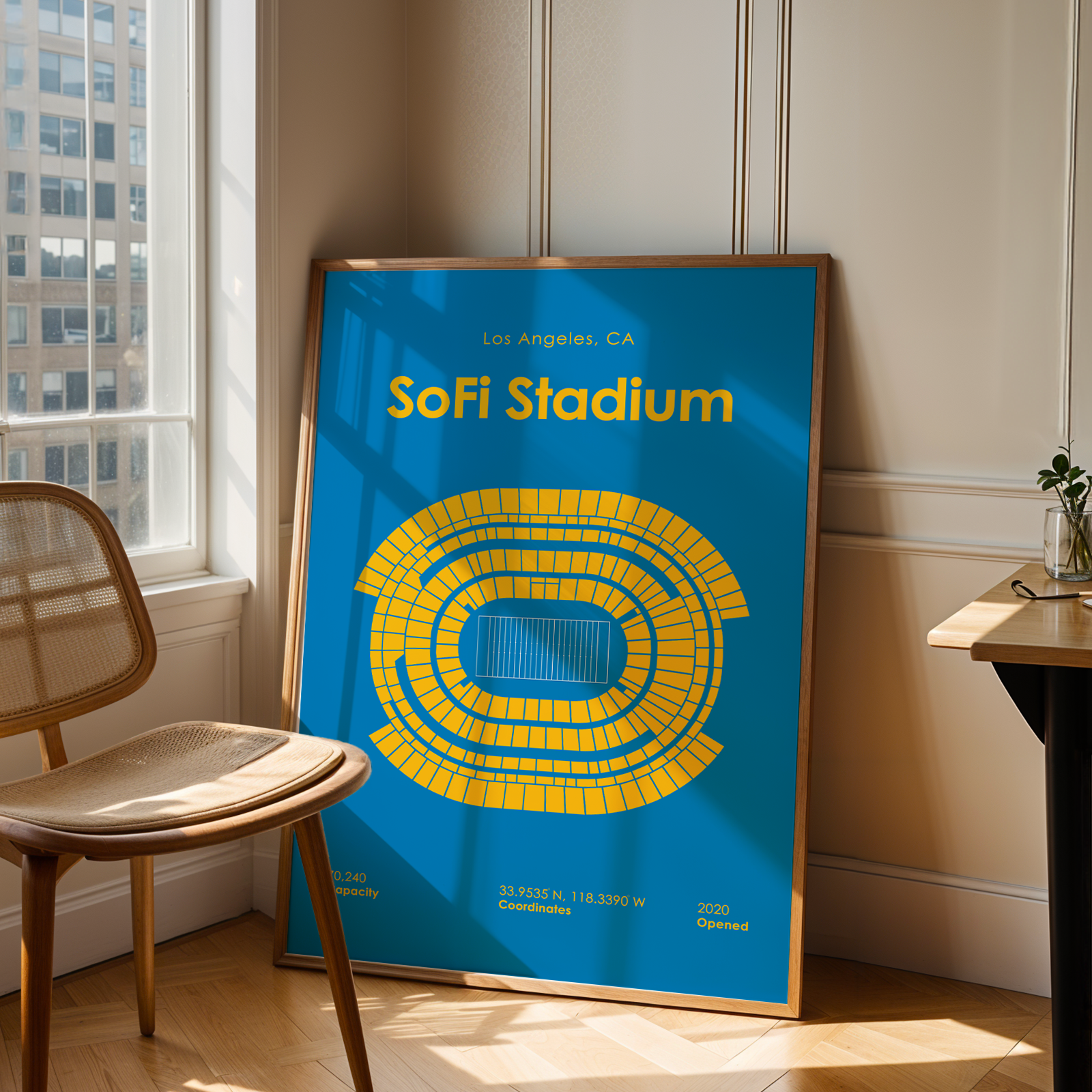 Framed poster of SoFi Stadium in a room with a chair and table.
