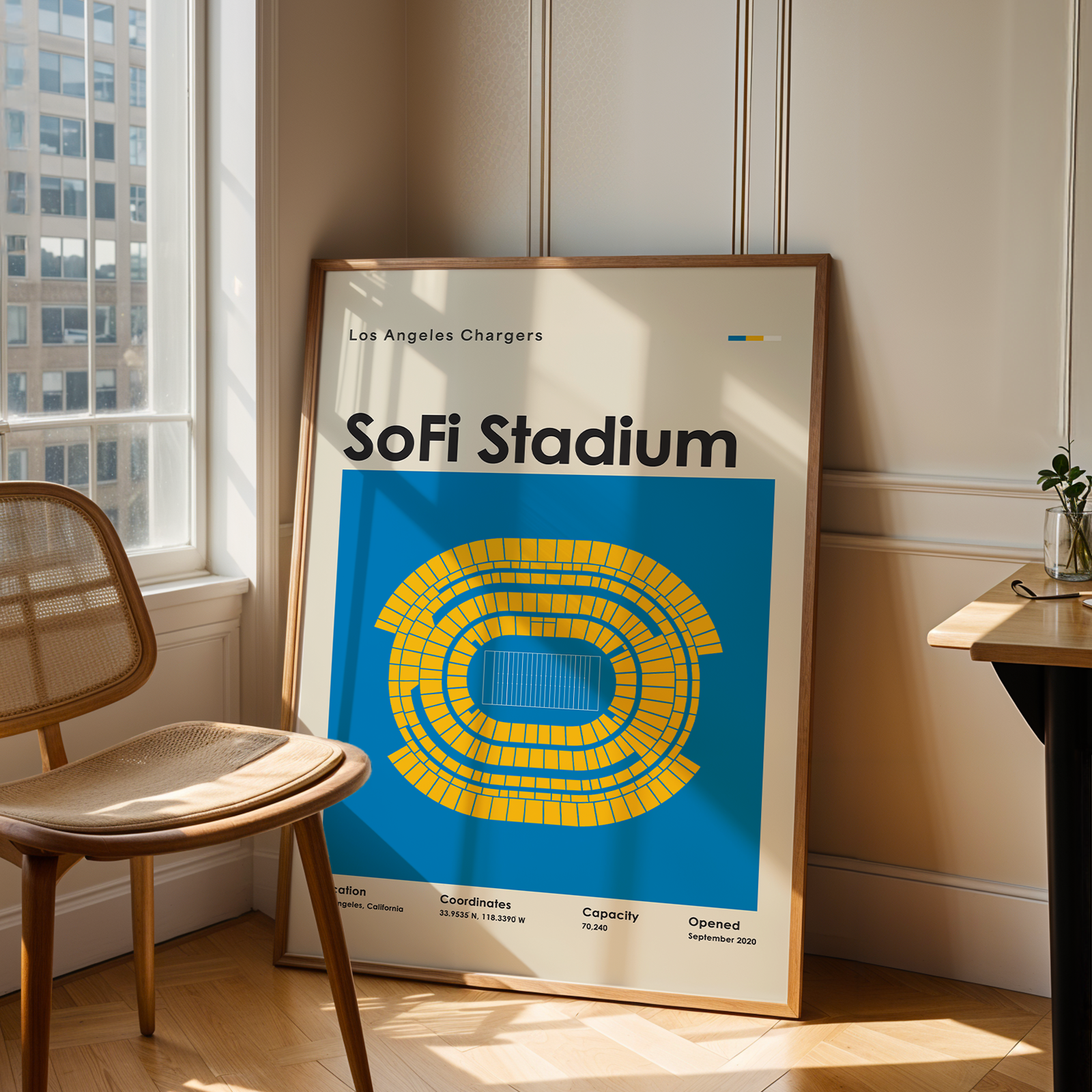 Framed poster of SoFi Stadium in a room with a chair and table.