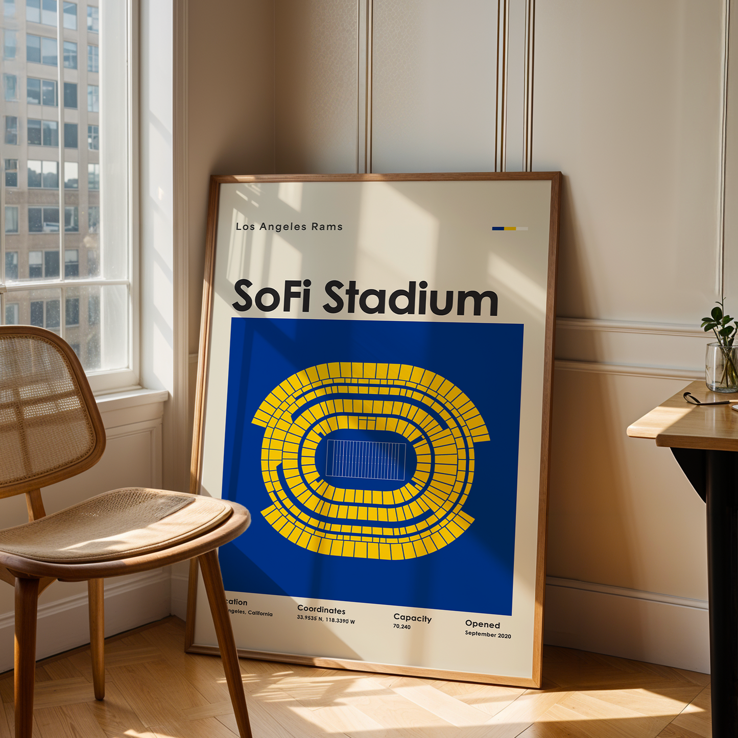 Framed poster of SoFi Stadium in a room with a chair and table.