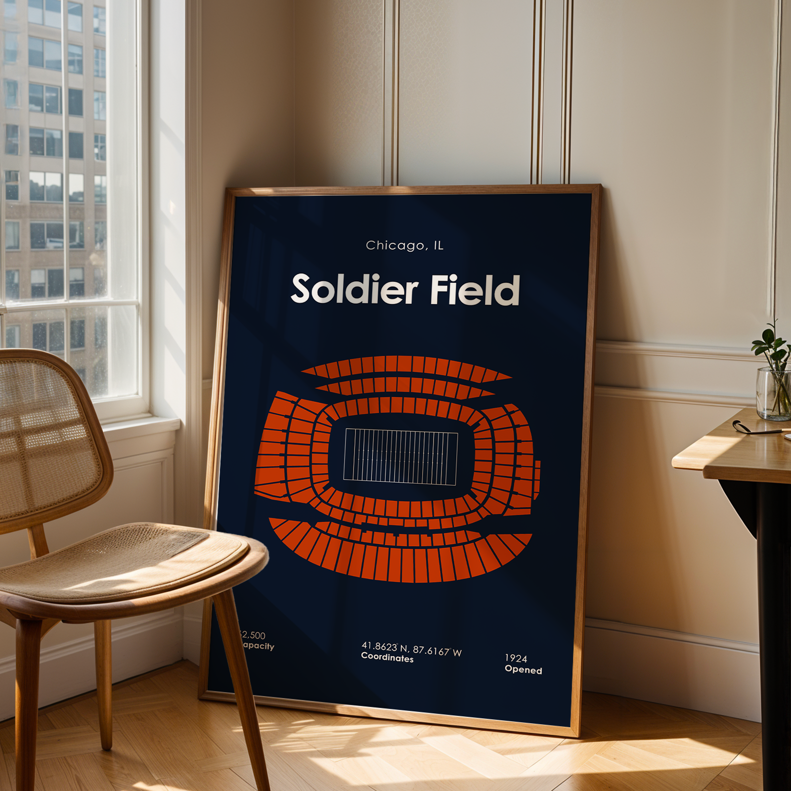 Poster of Soldier Field in Chicago, IL, leaning against a wall in a room with a chair and table.
